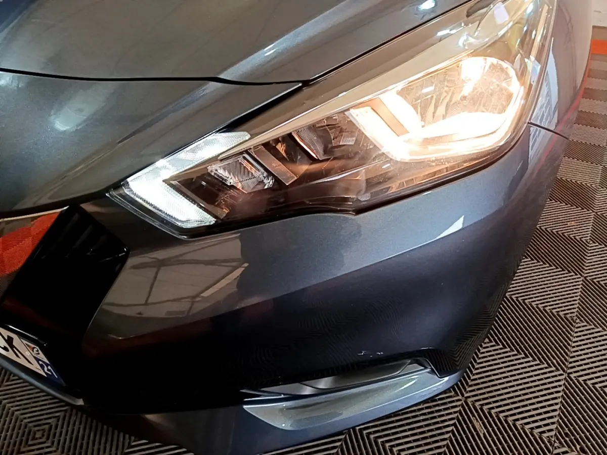 Gros plan sur l'avant droit gris foncé d'une Nissan Micra 2020 avec phare allumé et clignotant LED visible.