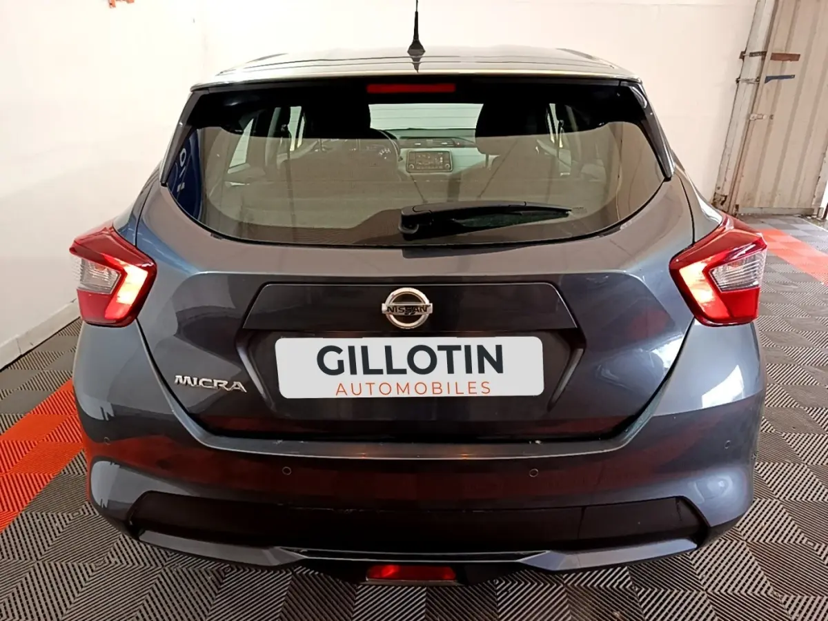 Vue arrière d'une Nissan Micra gris foncé avec feux arrière LED et logo Nissan visible sur un sol à damiers noir et rouge.