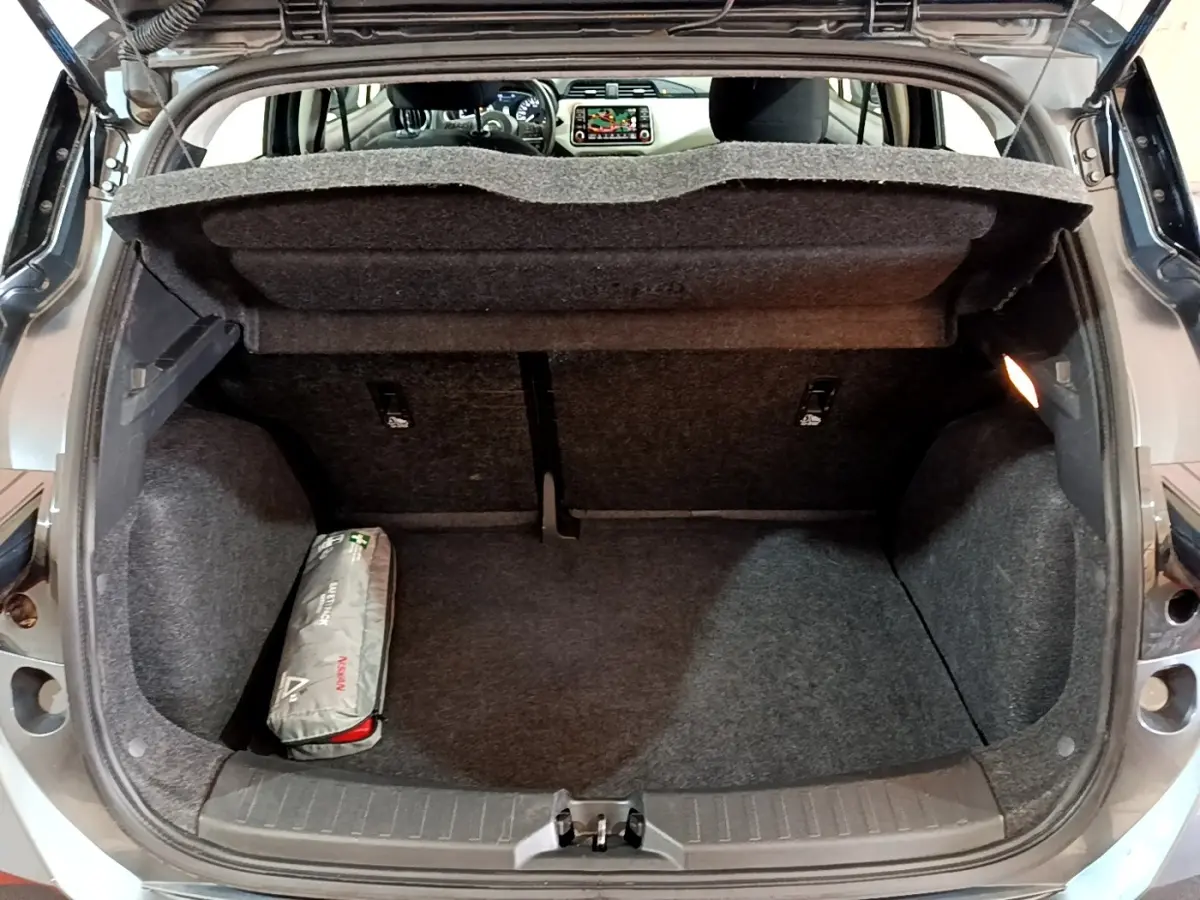 Coffre ouvert d'une Nissan Micra gris foncé, vue arrière montrant l'espace de chargement et un kit de secours.