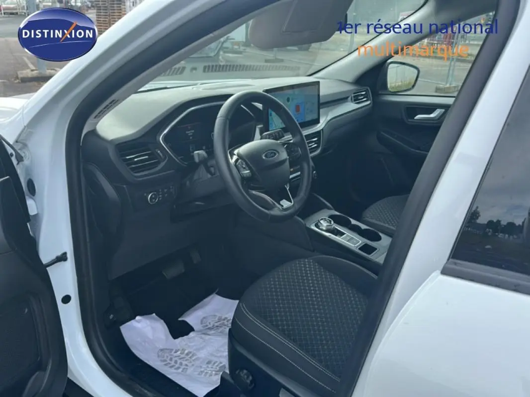 Vue intérieure côté conducteur du Ford Kuga blanc 2025, avec tableau de bord numérique et écran tactile central.