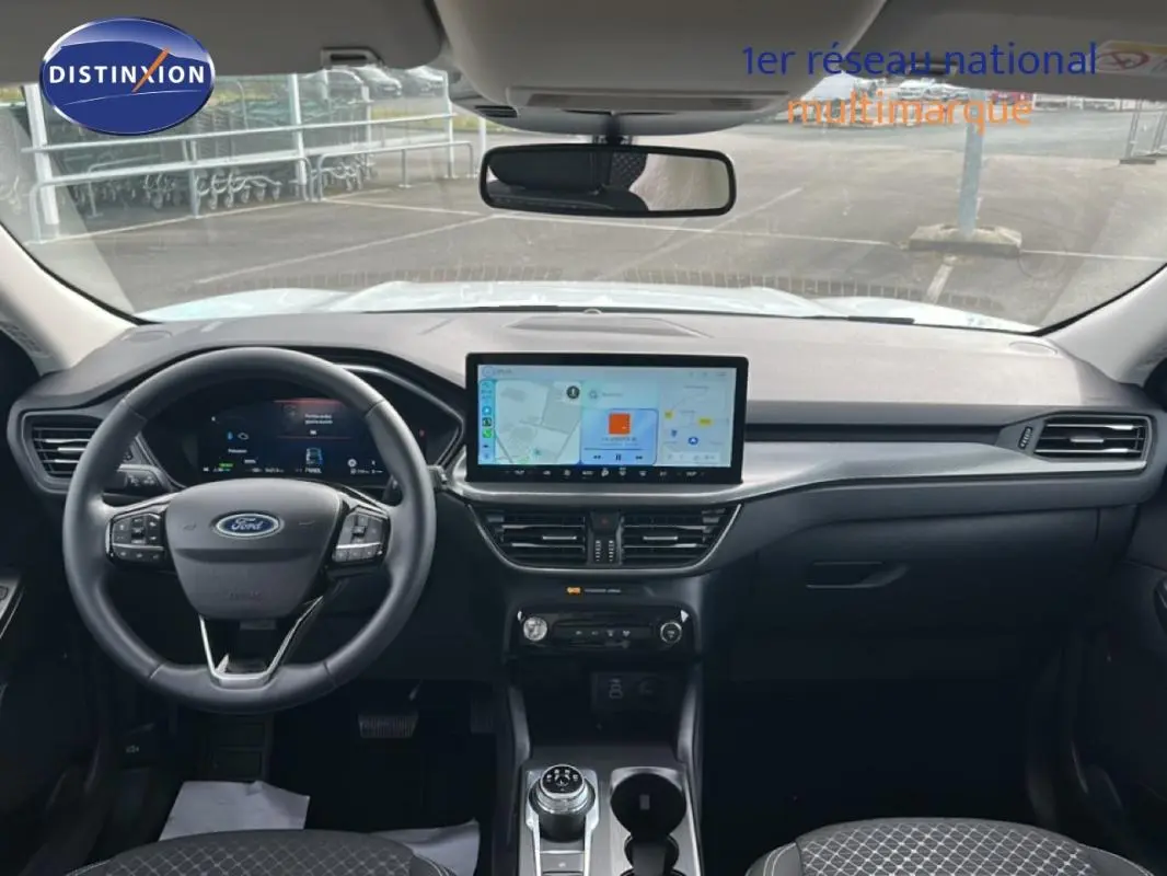 Vue intérieure frontale du tableau de bord noir du Ford Kuga blanc 2025 avec écran tactile central et volant multifonction.