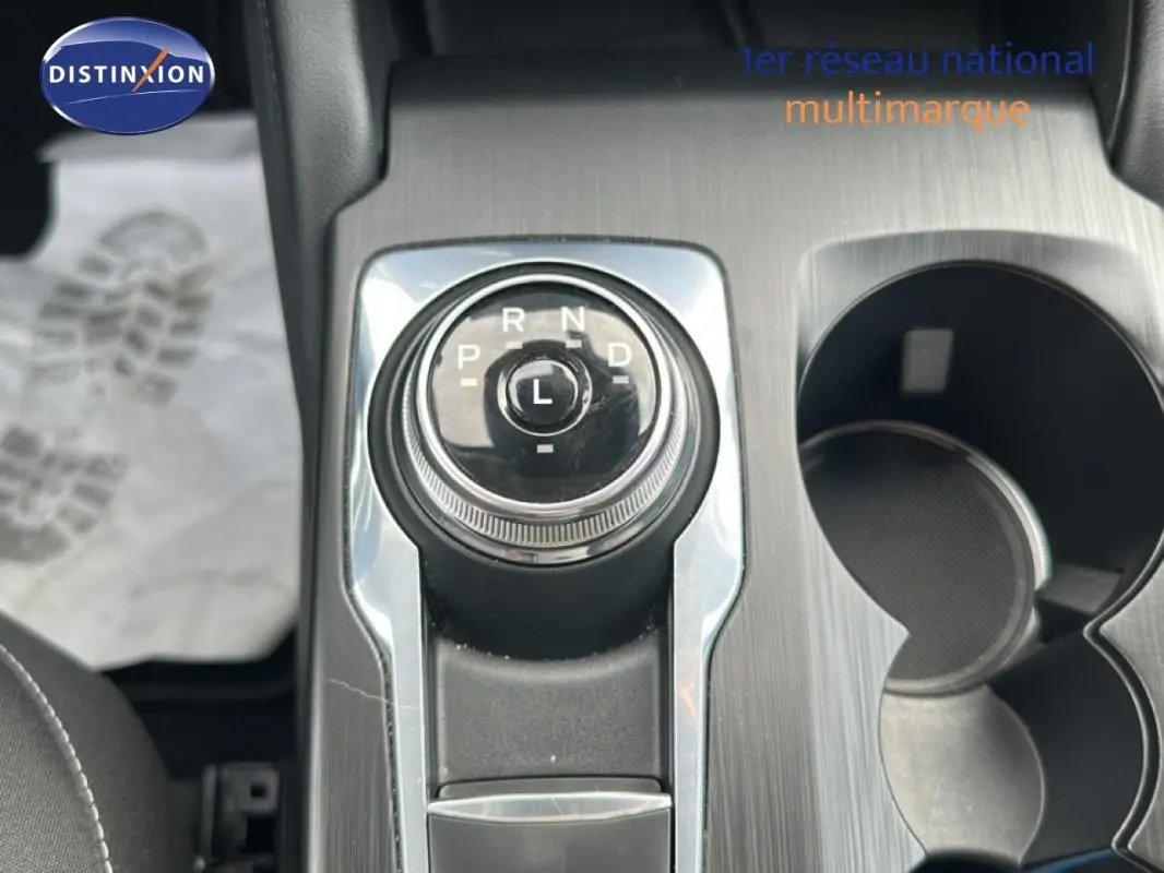 Gros plan sur la molette de boîte automatique du Ford Kuga blanc, avec porte-gobelets et console en finition métal brossé.