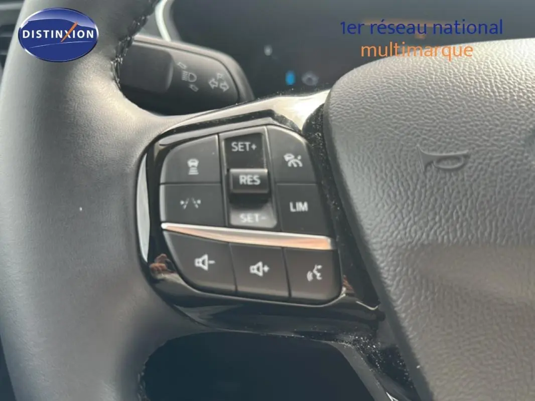 Gros plan sur les commandes au volant côté gauche du Ford Kuga blanc 2025 avec régulateur et limiteur de vitesse.