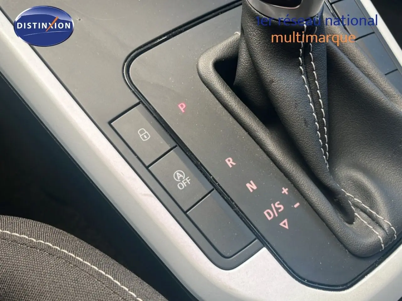 Gros plan sur la console centrale avec levier de vitesse automatique et coutures blanches sur tissu noir.