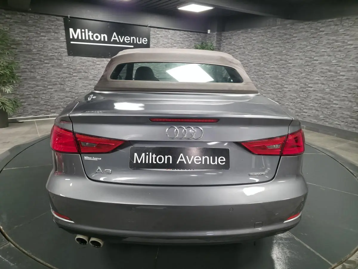 Vue arrière d'une Audi A3 Cabriolet gris foncé avec capote tissu beige et double sortie d'échappement chromée.