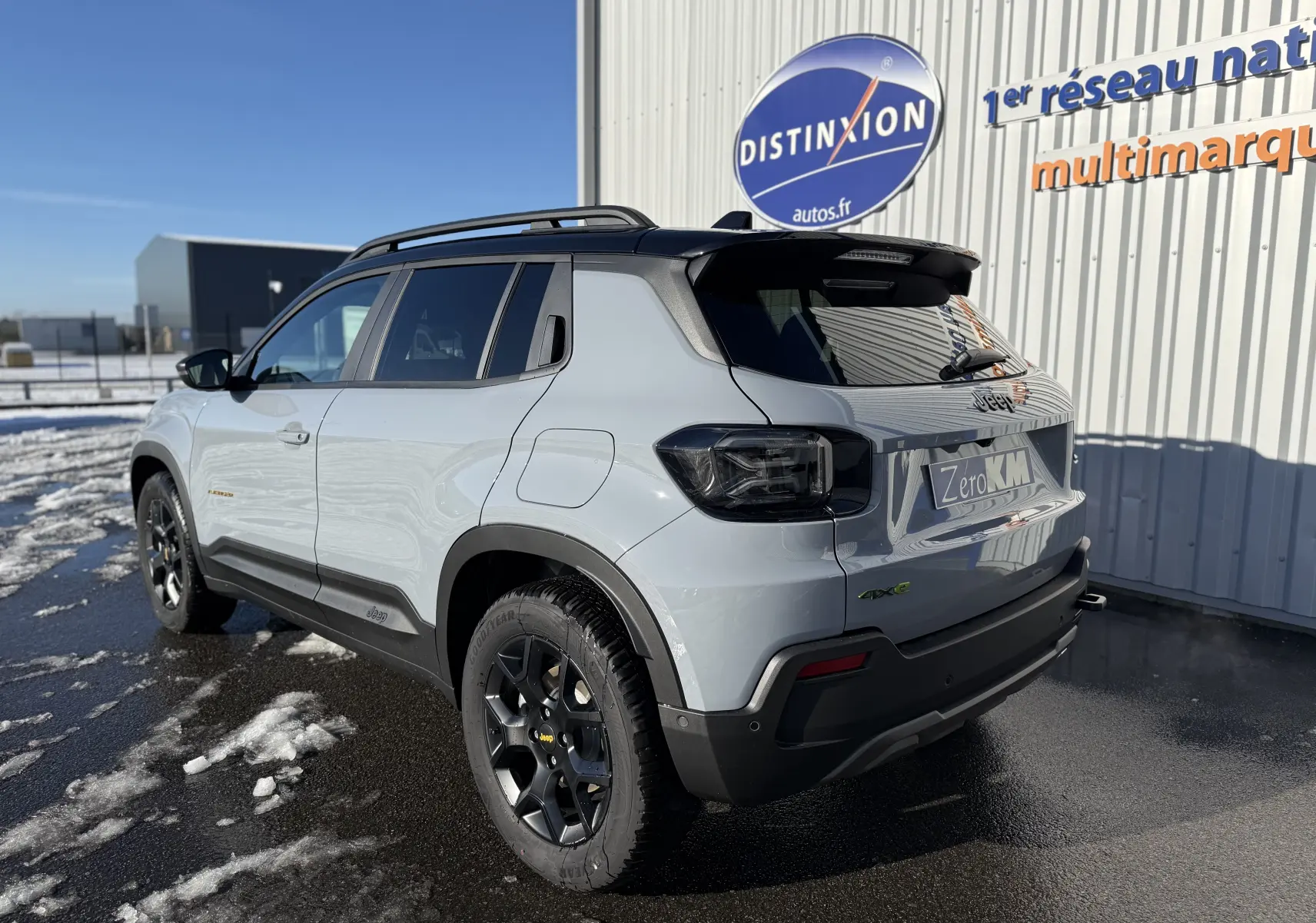 Jeep Avenger Storm Grey en 3/4 arrière droit, avec toit noir et jantes noires sur sol mouillé et enneigé.