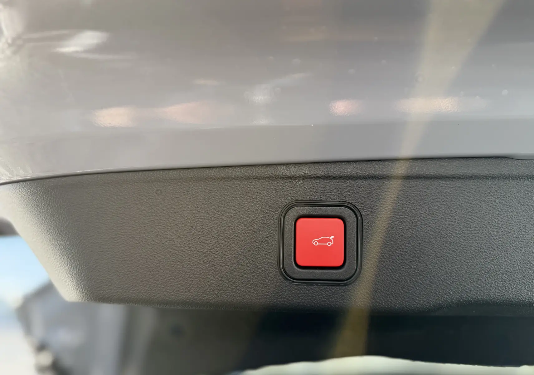 Bouton rouge de fermeture électrique du hayon sur le panneau intérieur d’un Jeep Avenger gris Storm Grey.
