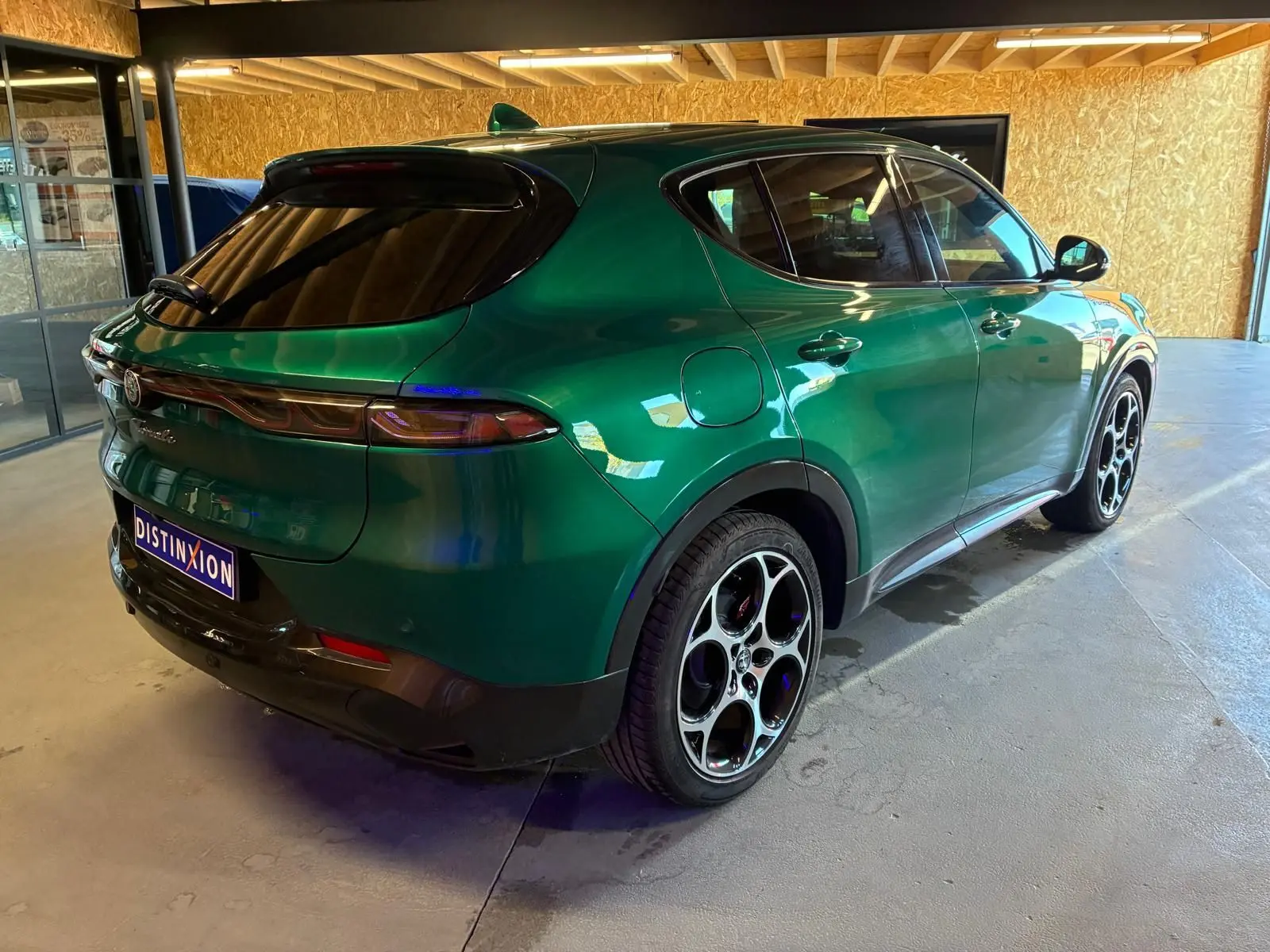 Vue 3/4 arrière droite d'une Alfa Romeo Tonale vert foncé avec jantes distinctives à cinq cercles, stationnée en intérieur.