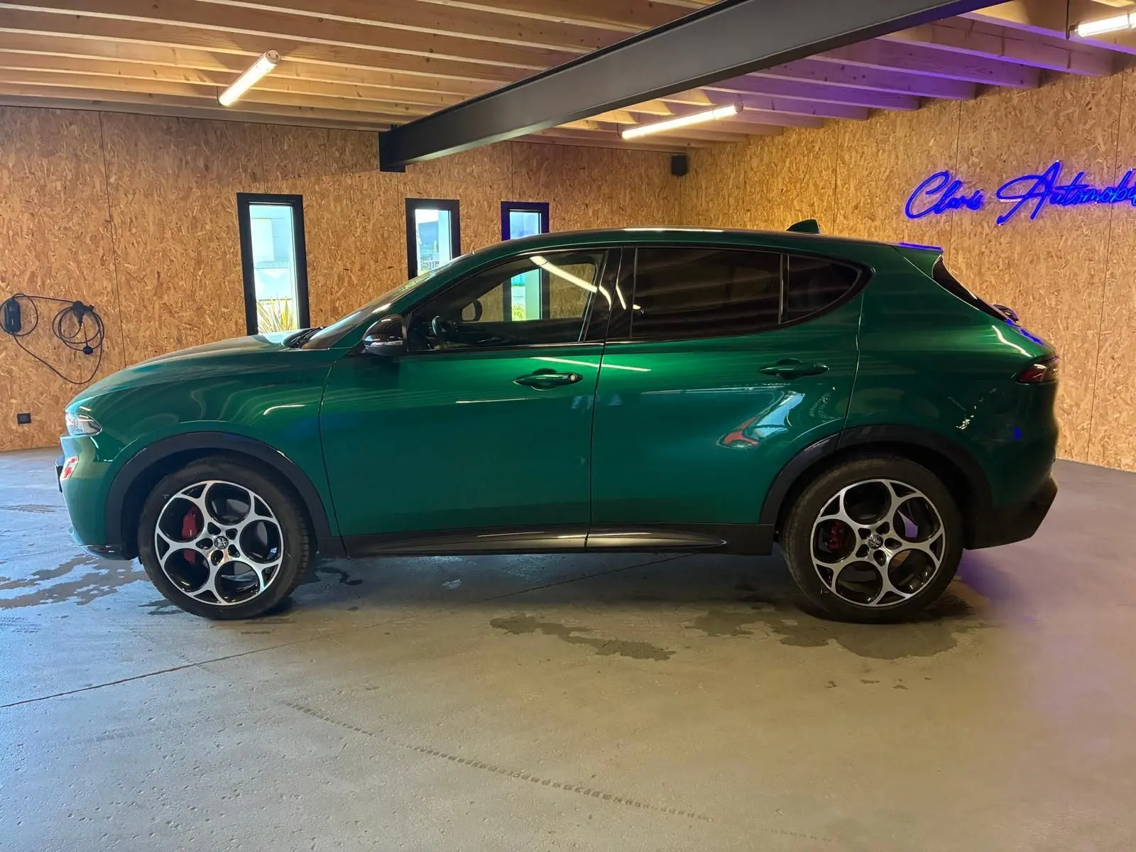 Vue de profil côté gauche d'un Alfa Romeo Tonale vert foncé avec jantes distinctives en intérieur bois.