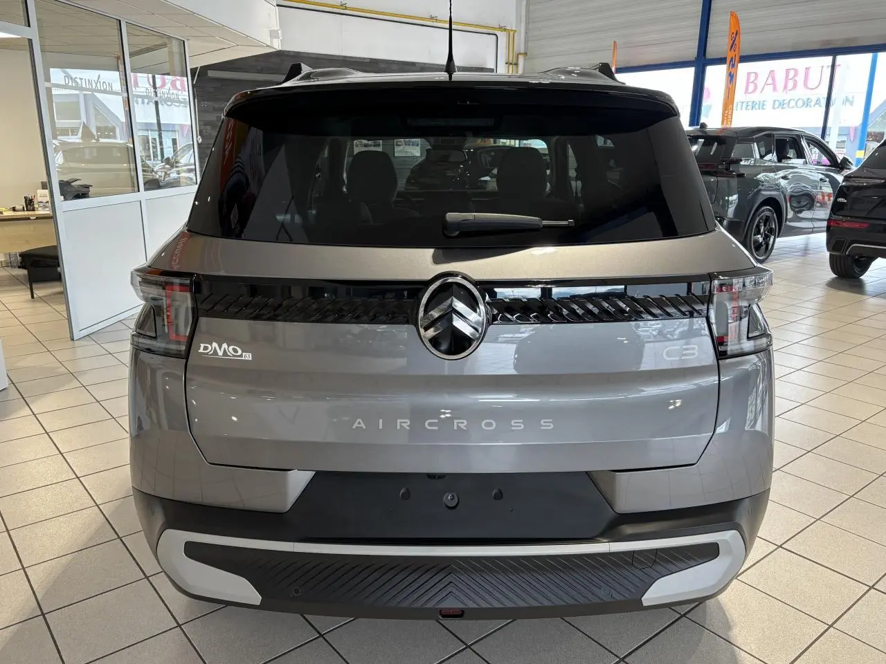 Vue arrière du Citroën C3 Aircross 2026 gris métallisé avec toit noir et feux arrière LED 3D en showroom.
