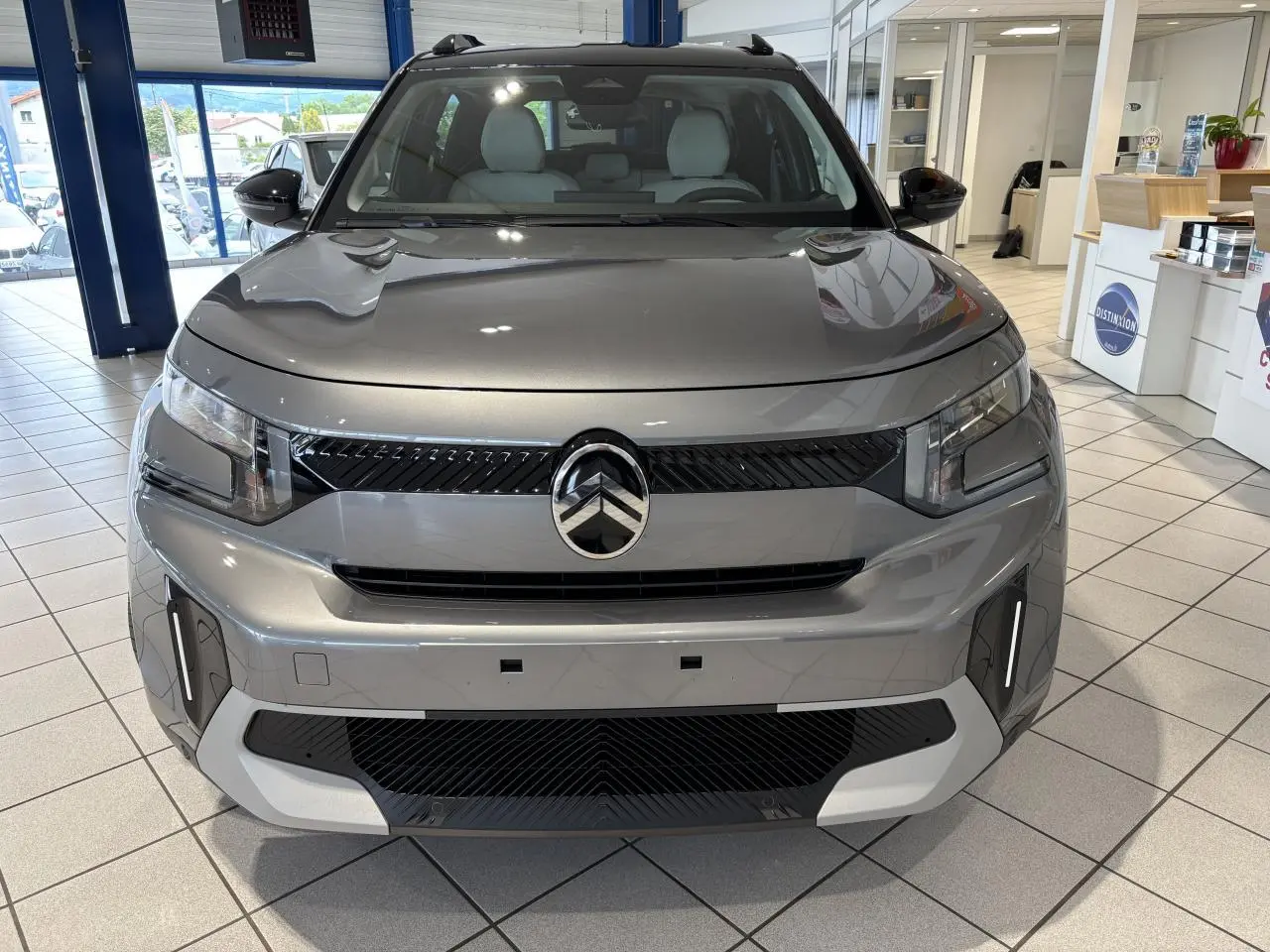 Vue avant d'un Citroën C3 Aircross 2026 gris métallisé avec toit noir et détails noirs brillants en showroom.