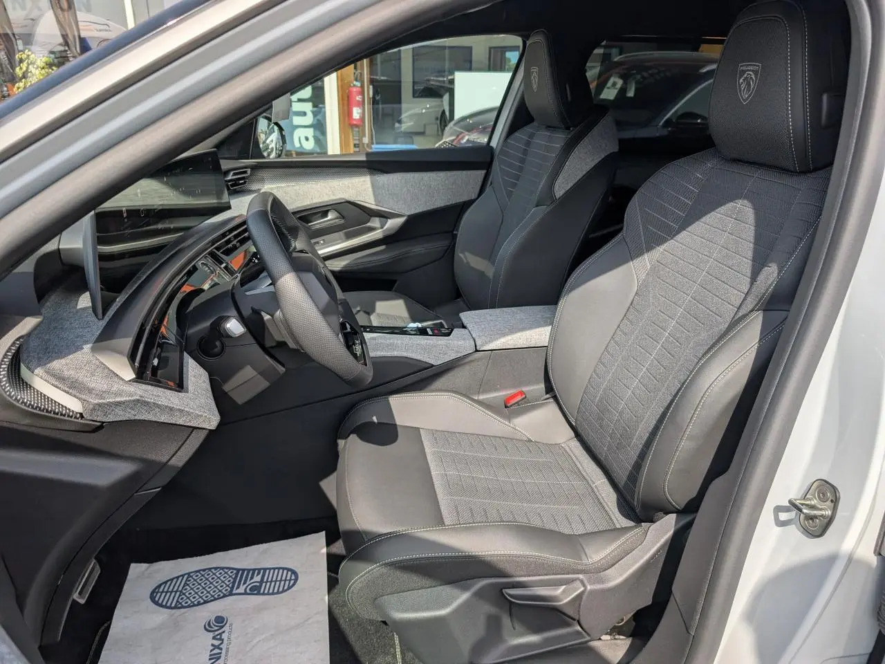 Vue intérieure côté conducteur du Peugeot 5008 blanc 2025, sièges tissu gris avec logo Peugeot brodé sur appuie-tête.