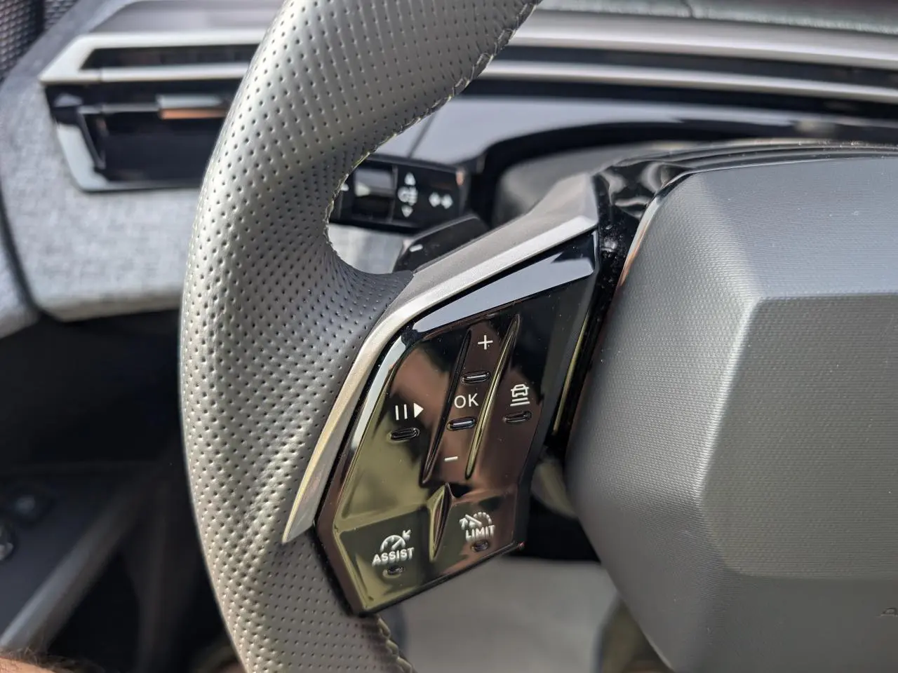 Gros plan sur les commandes gauche du volant perforé noir du Peugeot 5008 Hybrid 2025, avec boutons de régulateur et assistances.