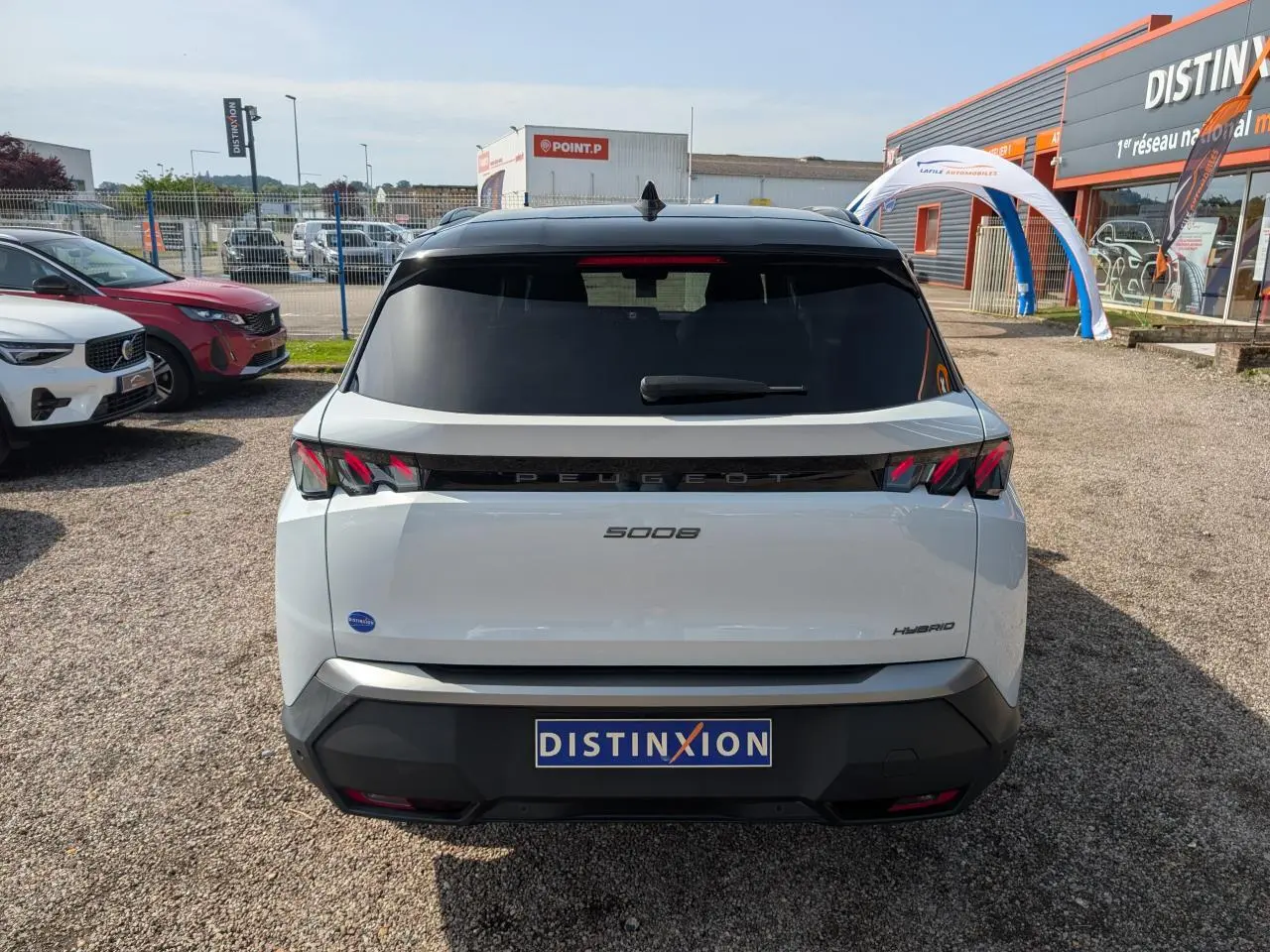 Vue arrière d’un Peugeot 5008 blanc hybride 2025 avec feux arrière 3 griffes et bandeau noir laqué entre les feux.