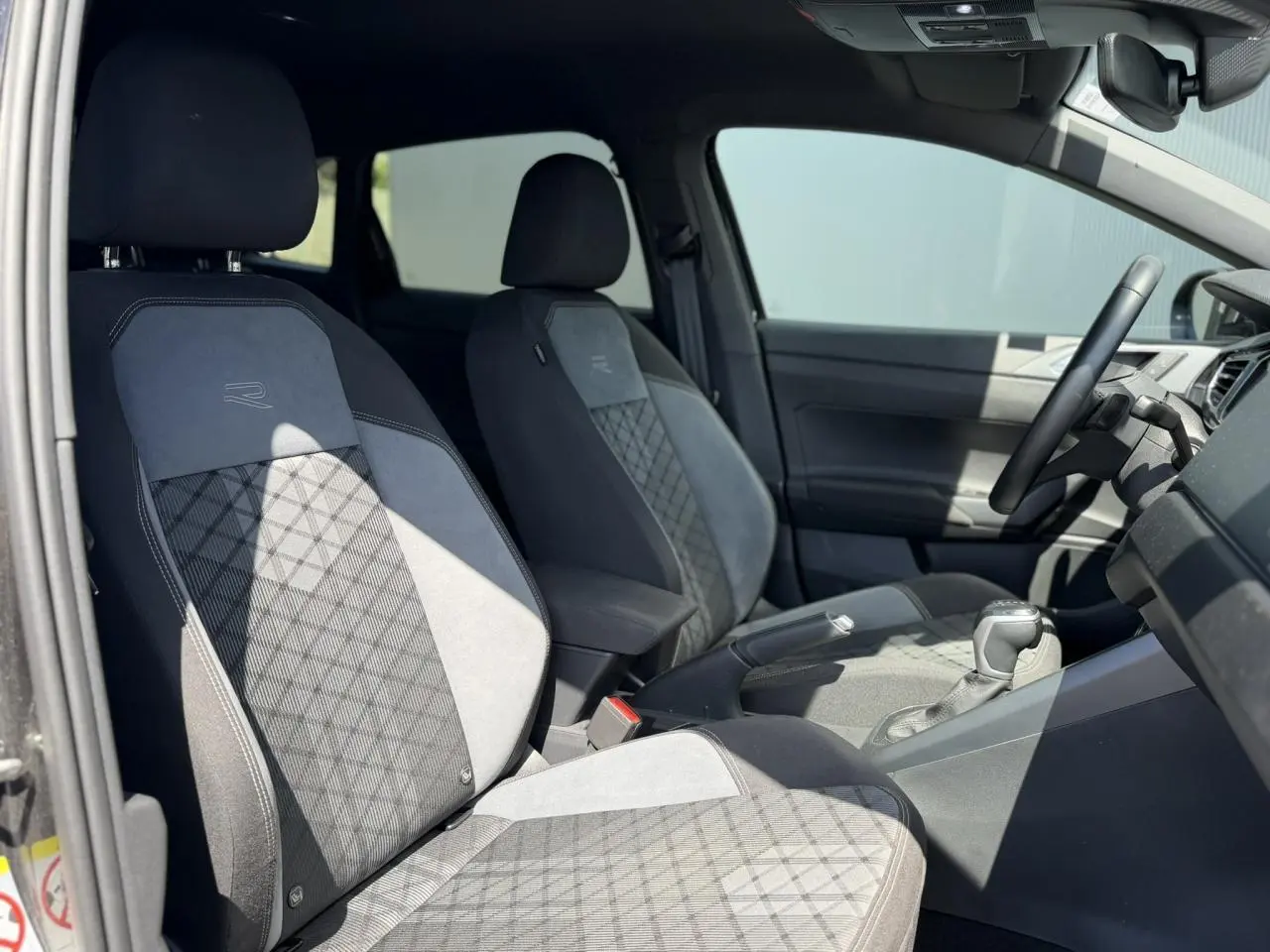 Vue intérieure côté gauche des sièges avant en tissu R-Line gris et noir du Volkswagen Taigo TSI 116 DSG 2025.