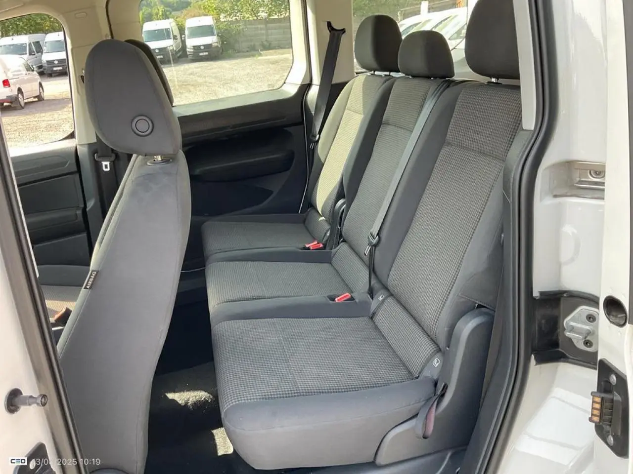 Vue intérieure côté droit sur les sièges arrière gris du Volkswagen Caddy blanc Candy avec porte coulissante ouverte.