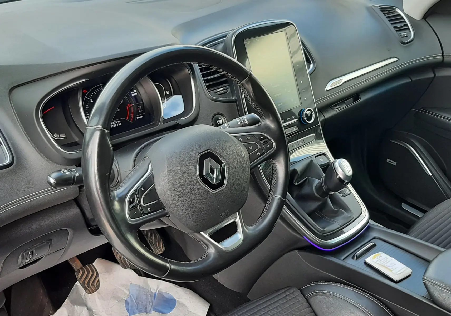 Coffre ouvert vu de l'arrière d'un Renault Scénic IV gris Cassiopée avec intérieur noir et tapis de coffre propre.