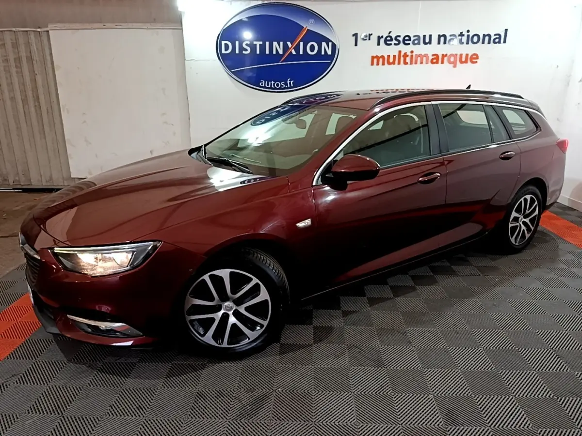 Opel Insignia break rouge vue 3/4 avant droit avec phares allumés dans un showroom intérieur.