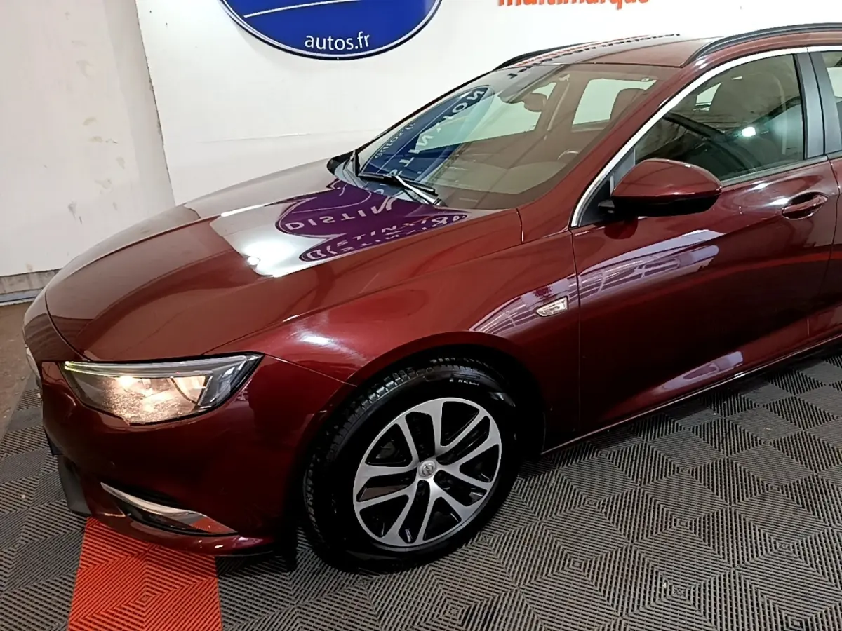 Vue 3/4 avant gauche d’une Opel Insignia rouge 2019 avec phares allumés et jantes alliage distinctives.