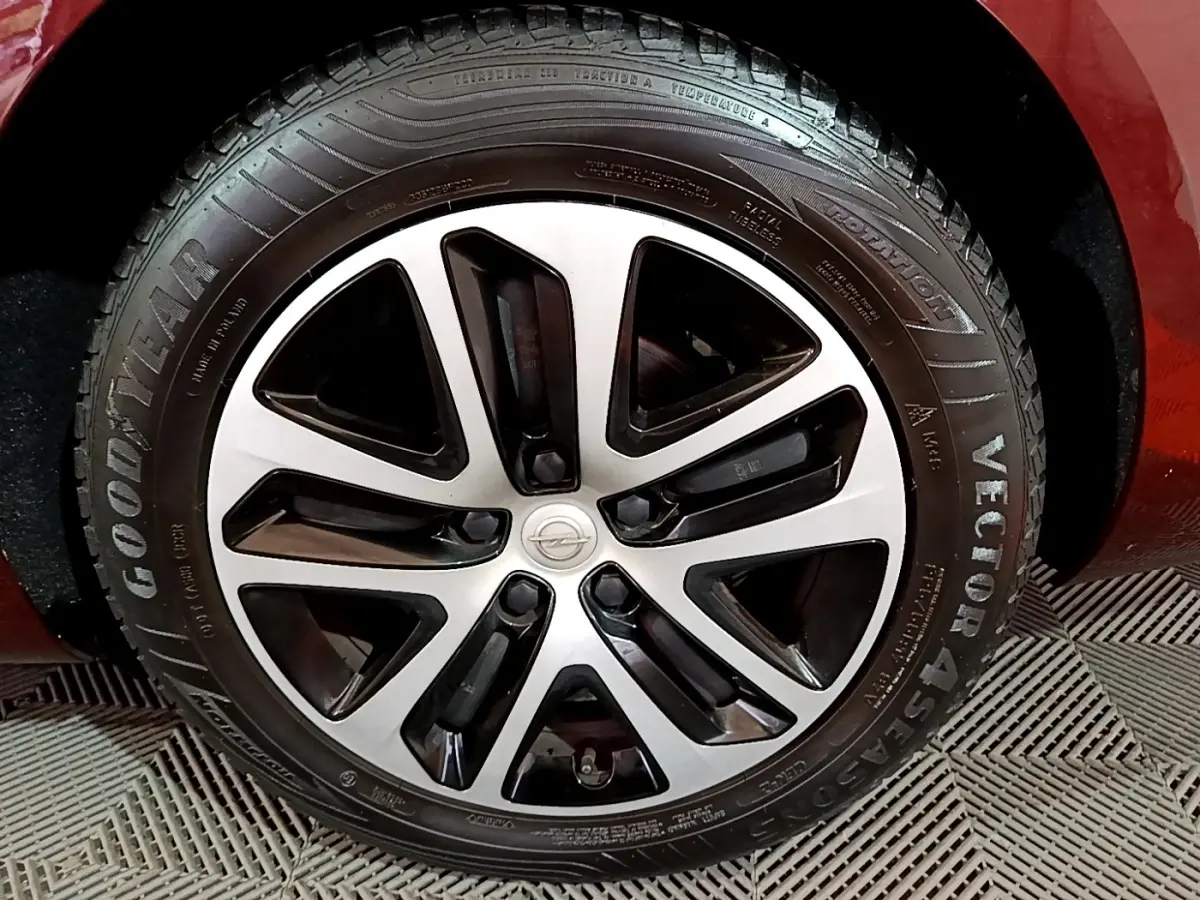 Gros plan sur la roue avant droite d’une Opel Insignia rouge, mettant en valeur la jante alliage bicolore et le pneu Goodyear.