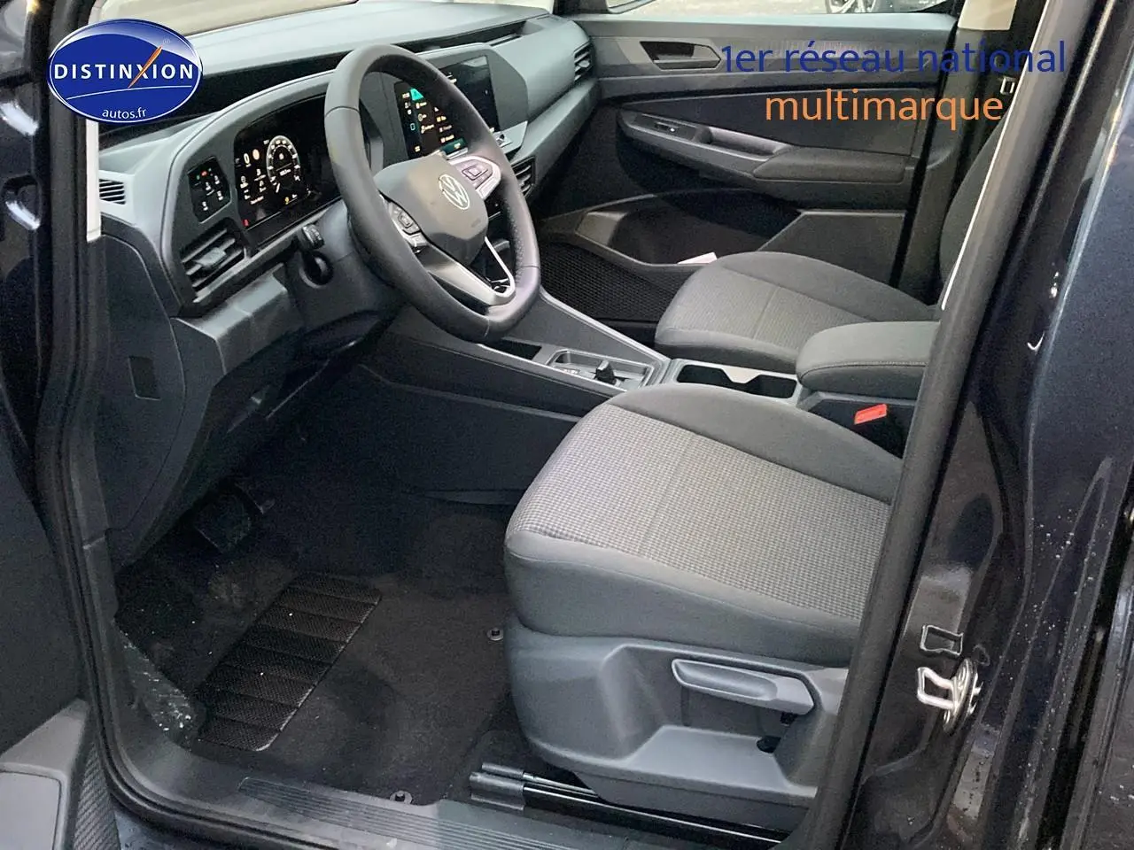 Vue intérieure côté conducteur du Volkswagen Caddy 2025 bleu métallisé, avec sièges tissu noir et tableau de bord moderne.