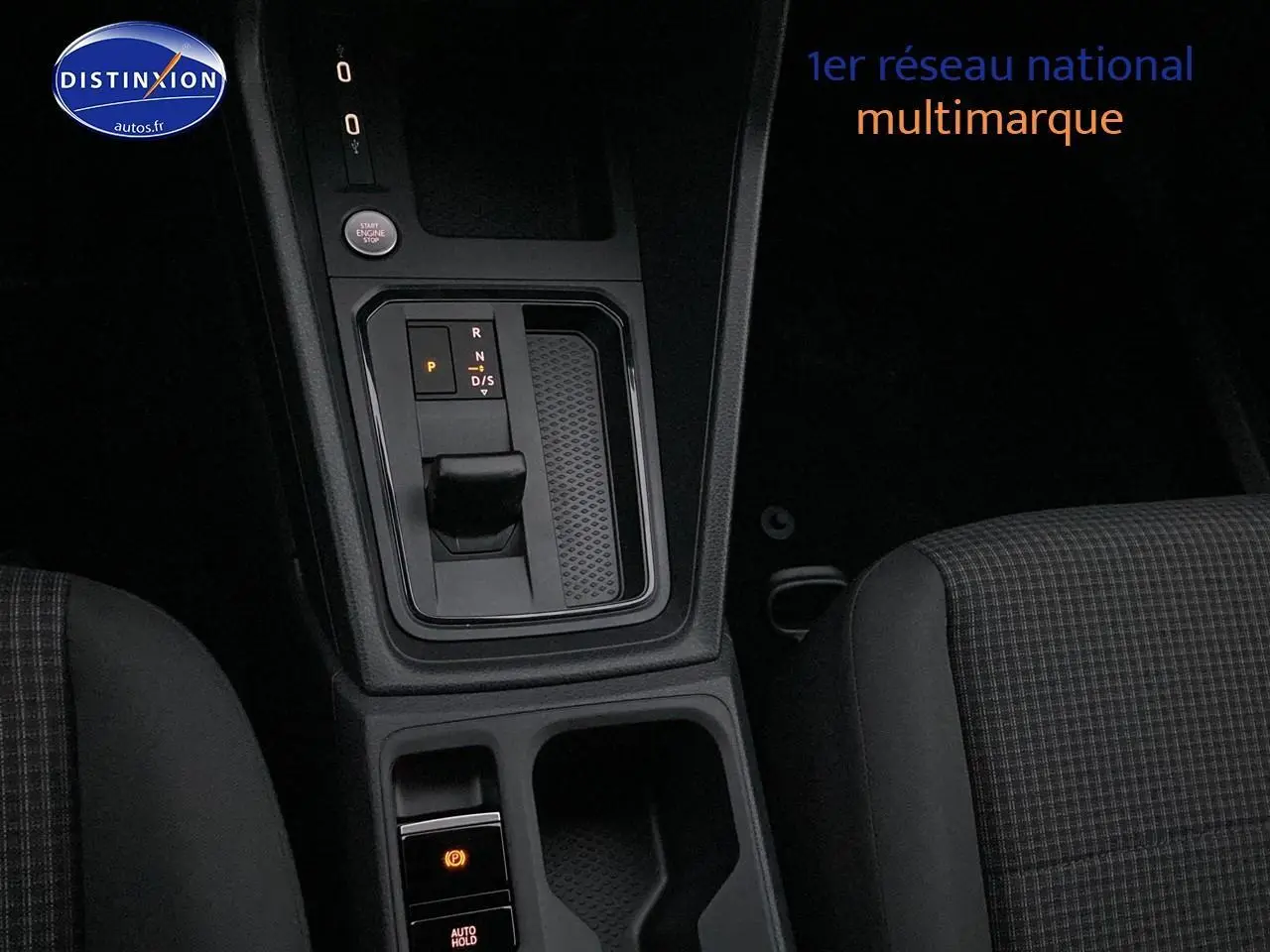 Vue rapprochée de la console centrale avec levier de vitesses automatique et sièges tissu noir à motifs du Volkswagen Caddy bleu métallisé.