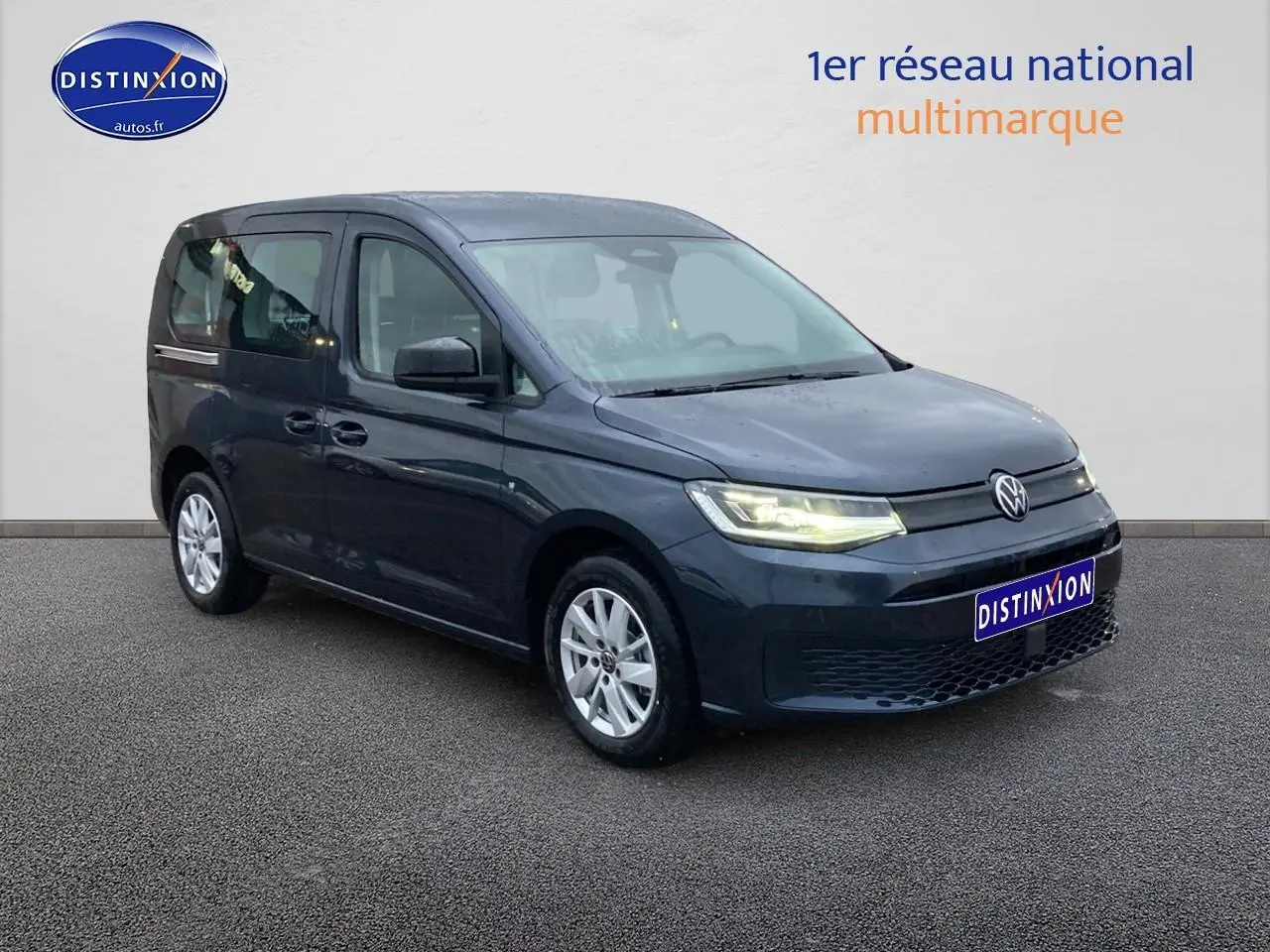 Volkswagen Caddy 2025 bleu métallisé en 3/4 avant droit avec phares allumés sur fond neutre.