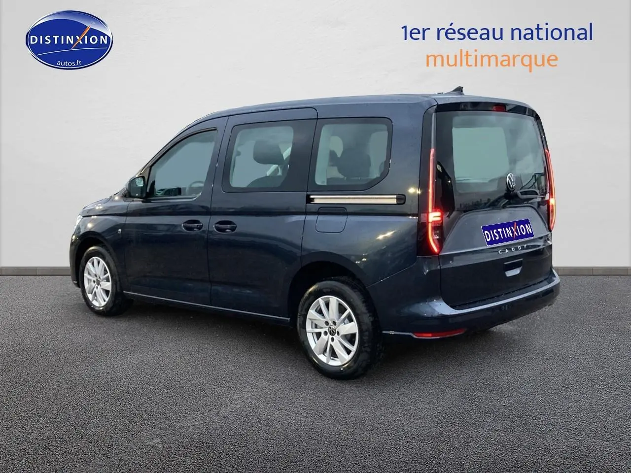 Vue 3/4 arrière droite d'un Volkswagen Caddy bleu métallisé avec feux arrière allumés sur fond neutre.