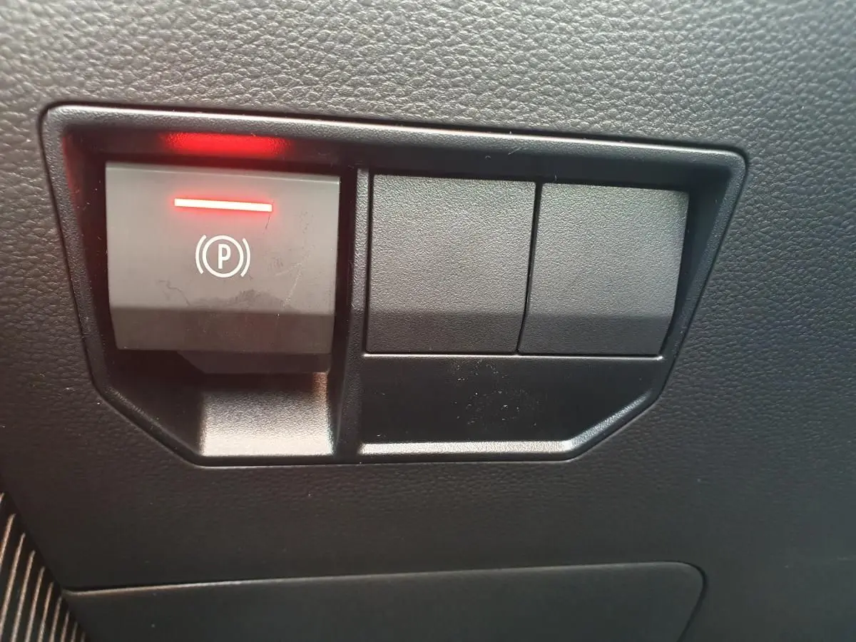 Gros plan sur le bouton de frein de stationnement électrique allumé dans l'habitacle noir du Dacia Dokker Van gris schiste.