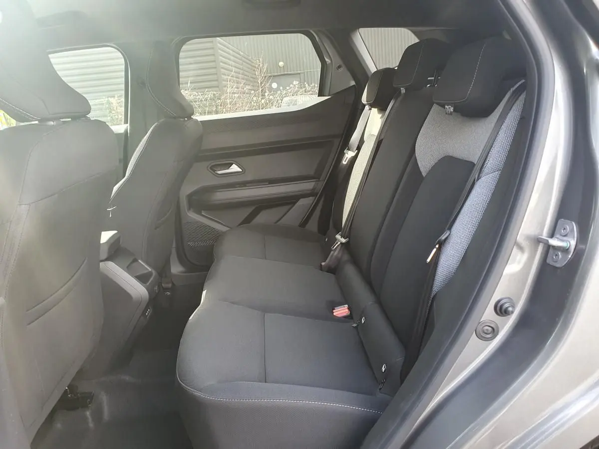 Vue intérieure côté droit sur la banquette arrière noire du Dacia Dokker Van gris schiste, avec appuie-têtes et ceintures visibles.