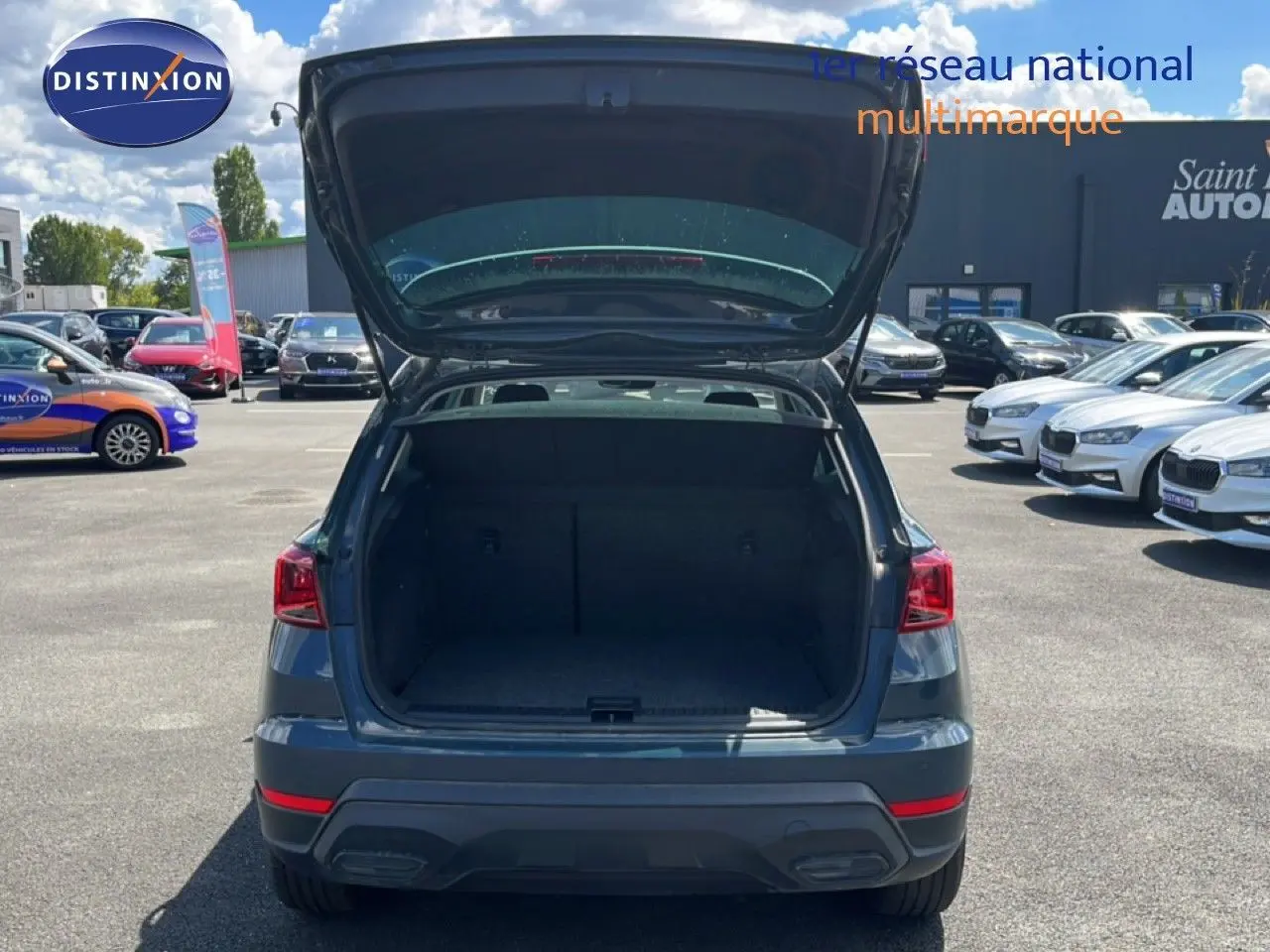 Vue arrière d'un SEAT Arona bleu Fjord avec coffre ouvert, toit blanc visible, sur un parking extérieur.