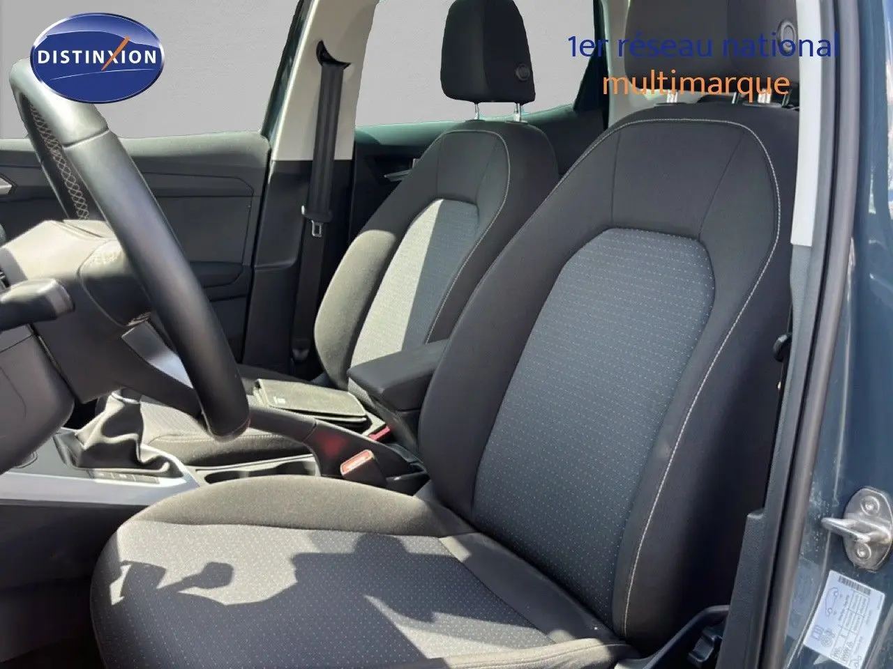 Vue intérieure côté conducteur du SEAT Arona 2025 bleu Fjord, montrant les sièges tissu gris noir et la boîte manuelle.