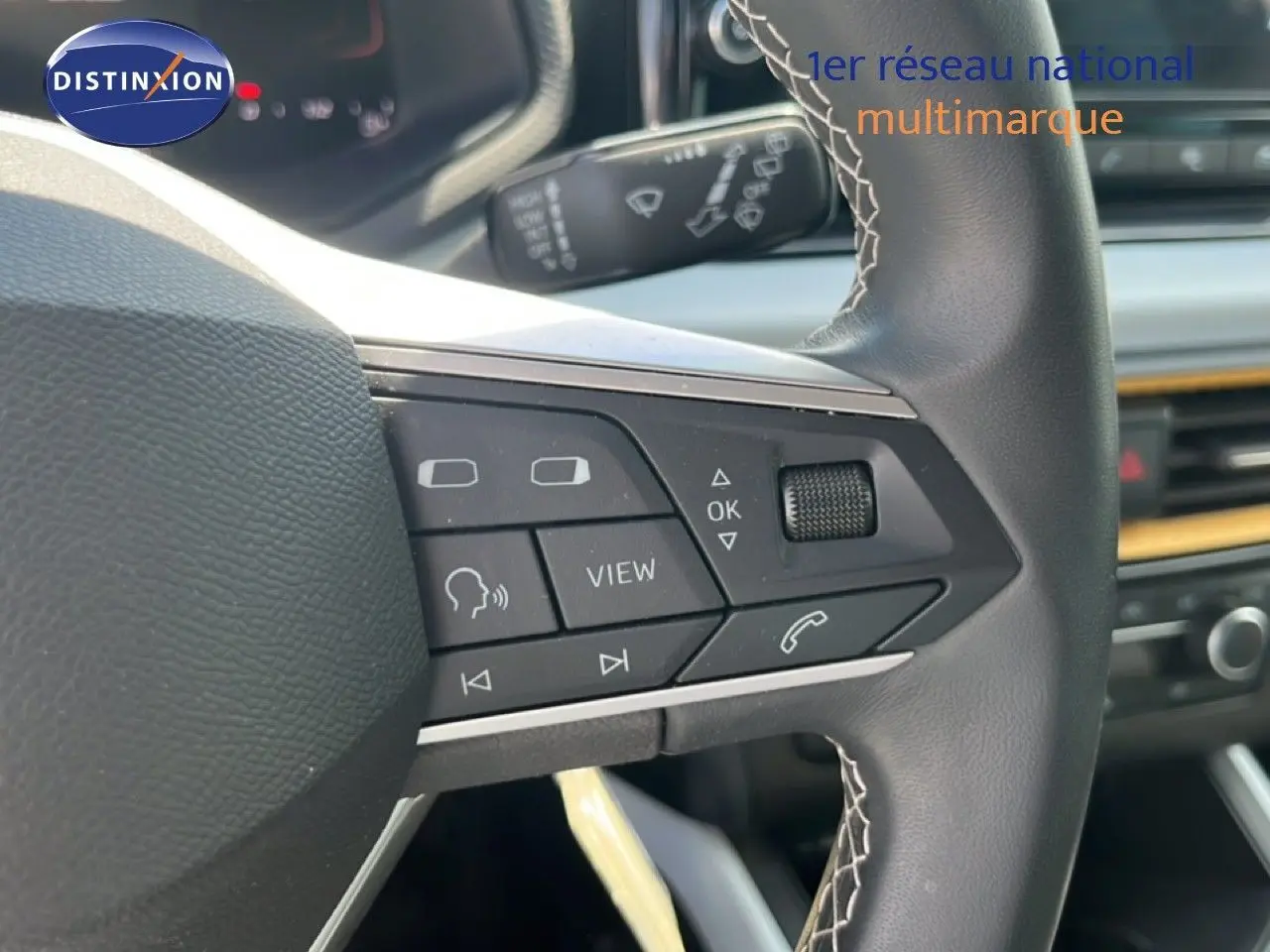 Gros plan sur le volant multifonction noir avec surpiqûres blanches du SEAT Arona 2025, intérieur gris et console visible.