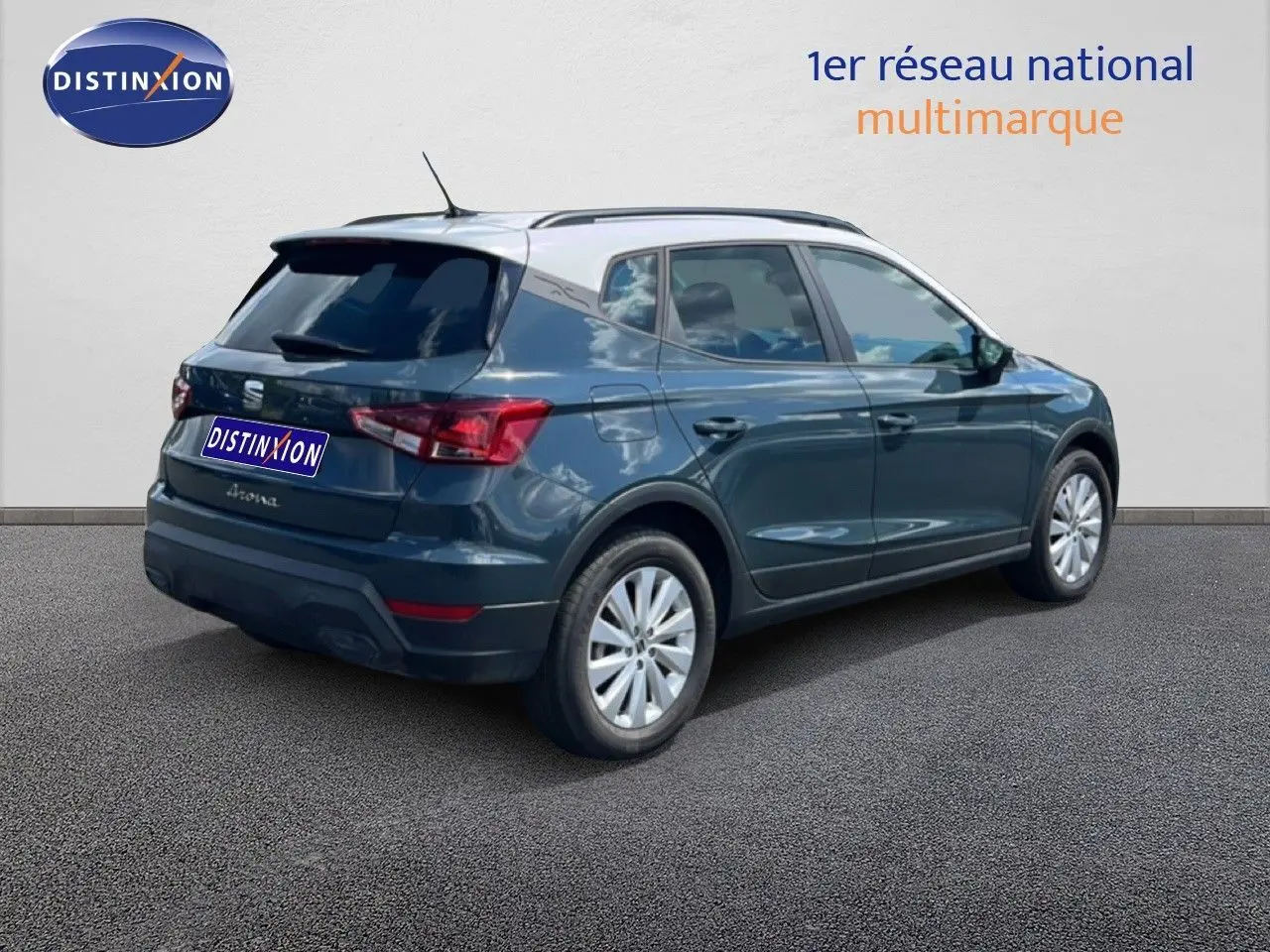 Vue 3/4 arrière droite d'une SEAT Arona bleu Fjord avec toit blanc, stationnée sur sol gris devant un mur clair.