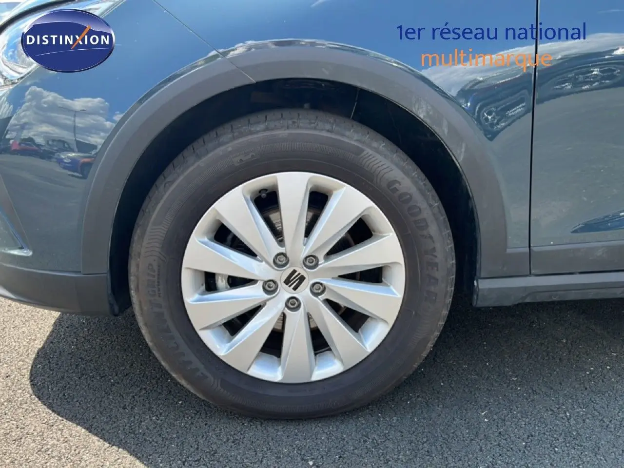 Gros plan sur la roue avant gauche d’un SEAT Arona bleu Fjord avec jante argentée et logo central Seat.