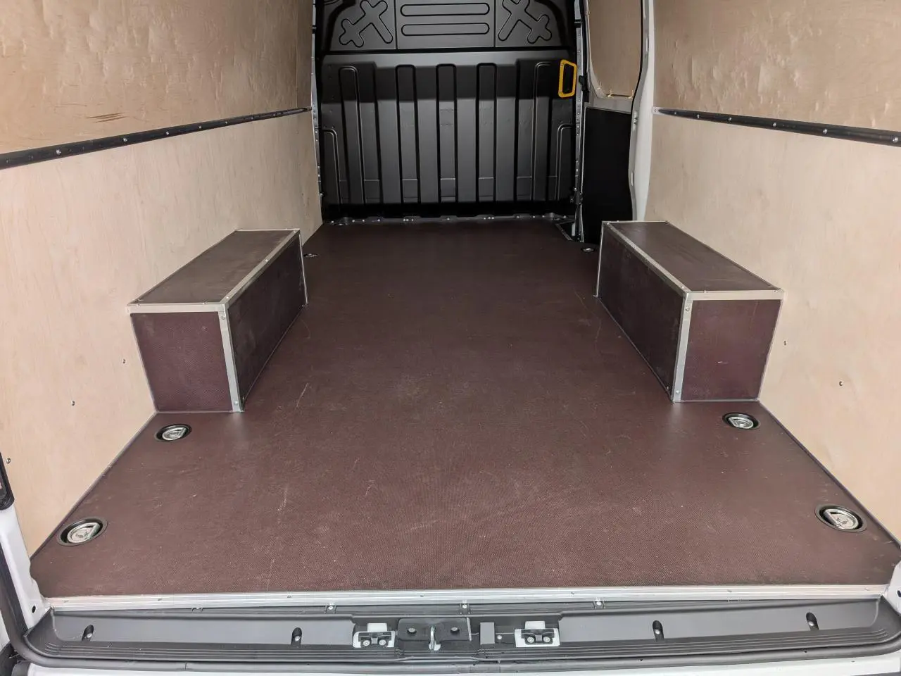Vue intérieure arrière du fourgon Iveco Daily blanc avec plancher antidérapant marron et habillages latéraux en bois clair.