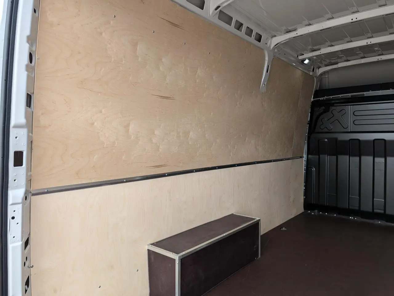 Vue intérieure côté droit du coffre d’un Iveco Daily blanc avec habillage bois clair et plancher foncé antidérapant.