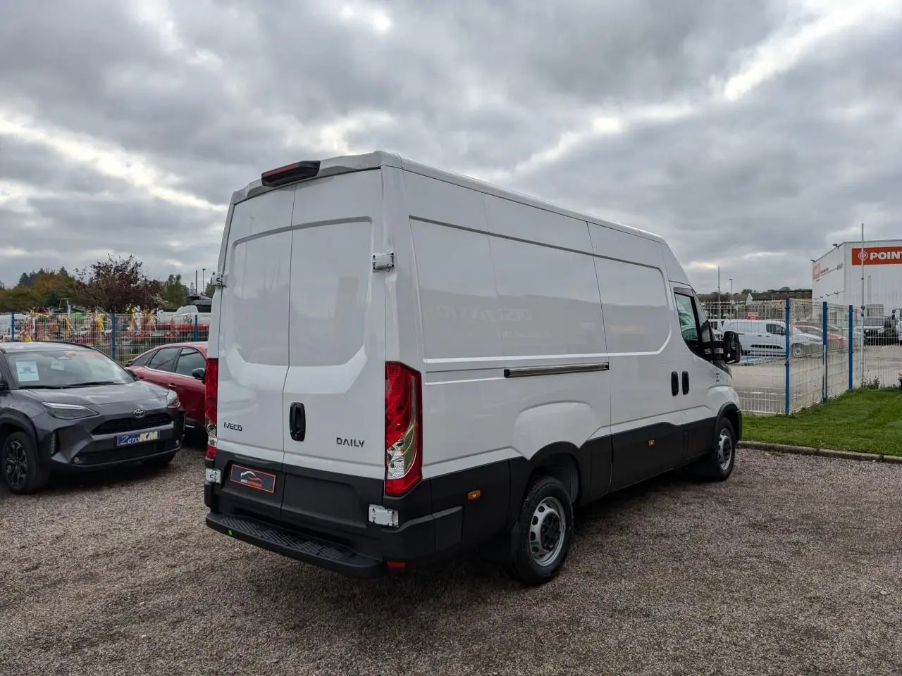 IVECO Daily blanc vu 3/4 arrière droit, portes arrière fermées et calandre noire visible sur parking.