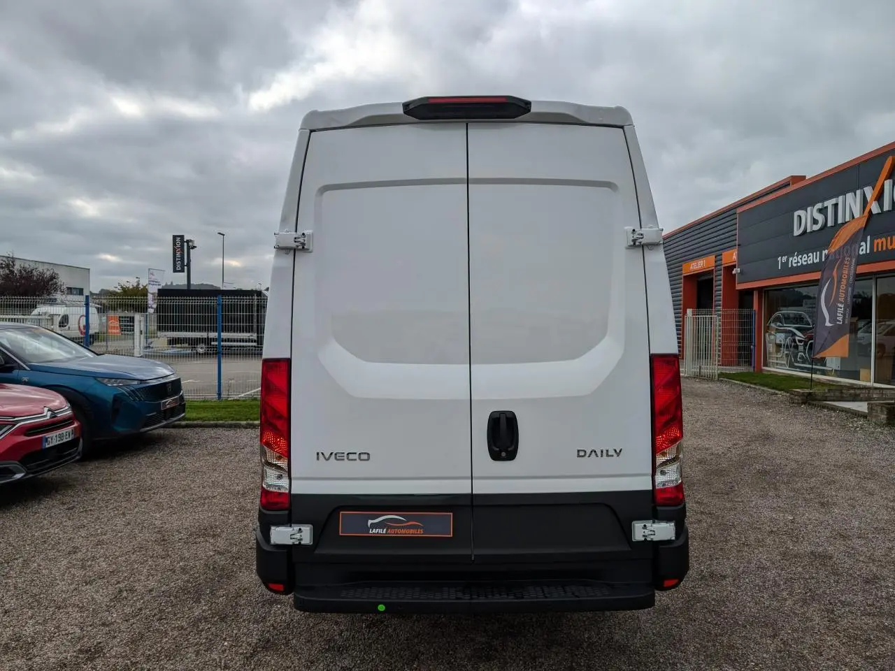Vue arrière d’un utilitaire Iveco Daily blanc avec portes battantes et feux arrière rouges visibles.
