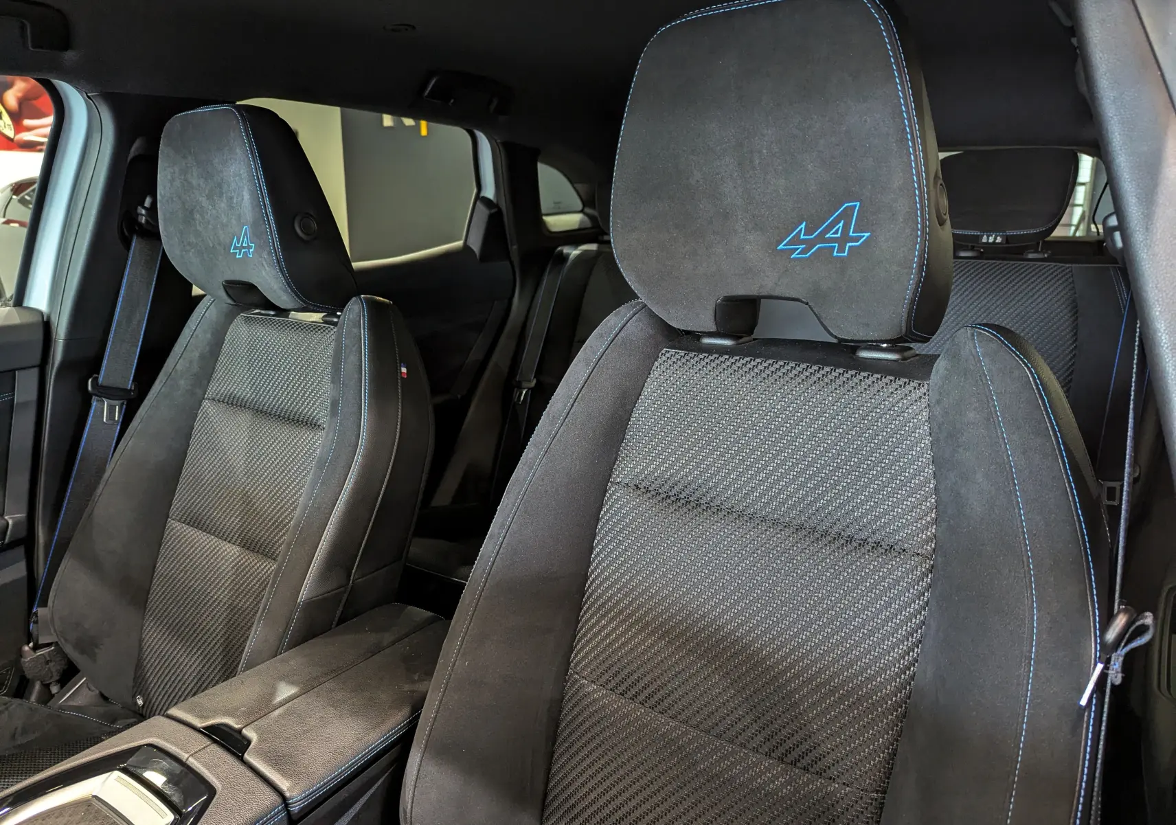 Vue rapprochée des sièges avant noirs avec surpiqûres bleues et logo Alpine brodé dans l'habitacle du Renault Austral 2023.