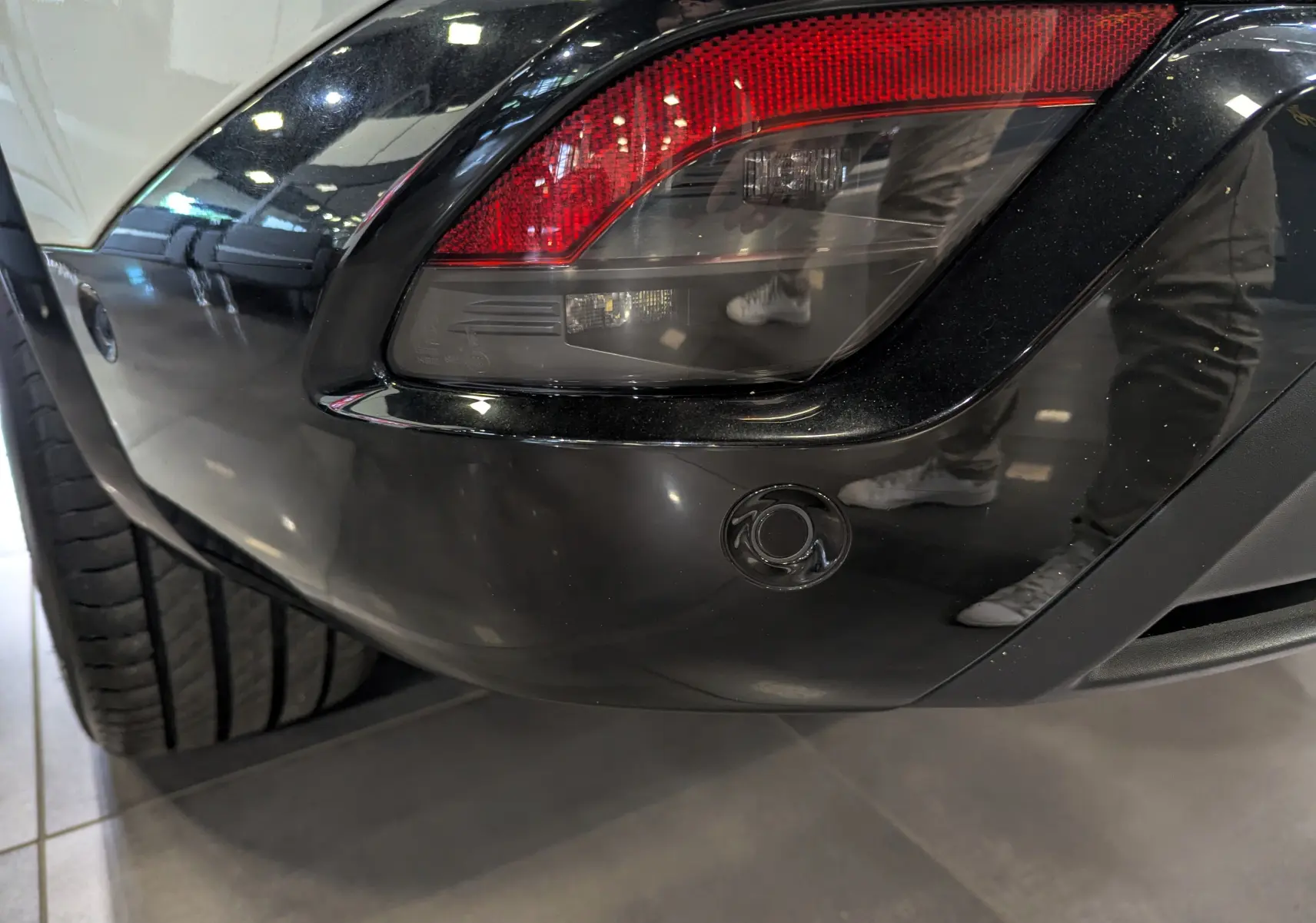 Gros plan sur le feu arrière droit noir brillant du Renault Austral blanc nacré avec pare-chocs noir et capteur de recul.