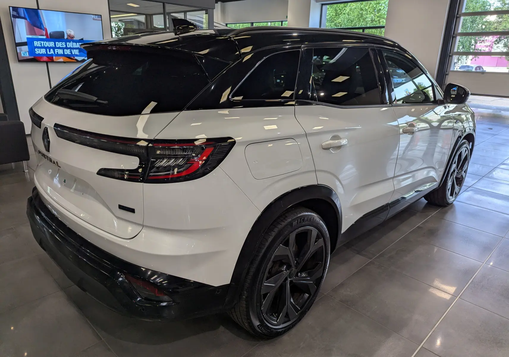 Vue 3/4 arrière droite du Renault Austral blanc nacré avec toit noir et jantes noires dans un showroom.