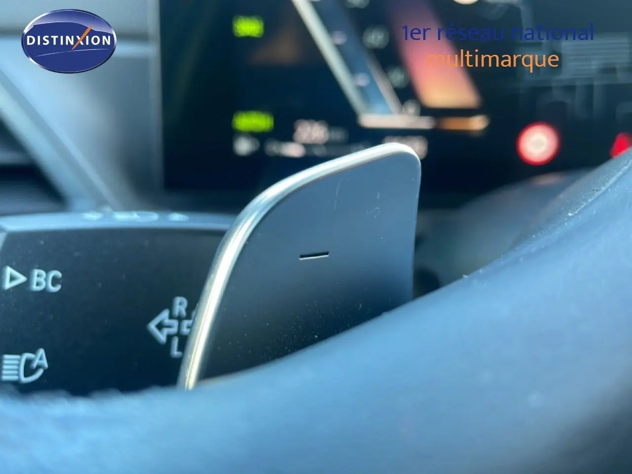 Gros plan sur la palette de changement de vitesse côté droit du volant d’une BMW Série 3 Touring noire, avec tableau de bord flou en arrière-plan.