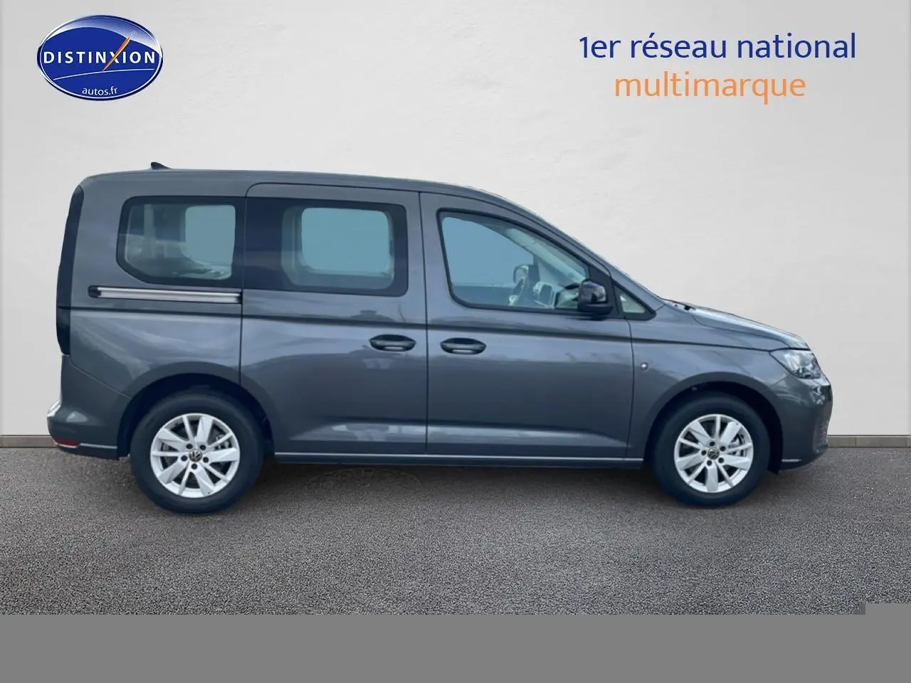 Profil droit d'un Volkswagen Caddy gris indien 2025 avec barres de toit et jantes alliage visibles.