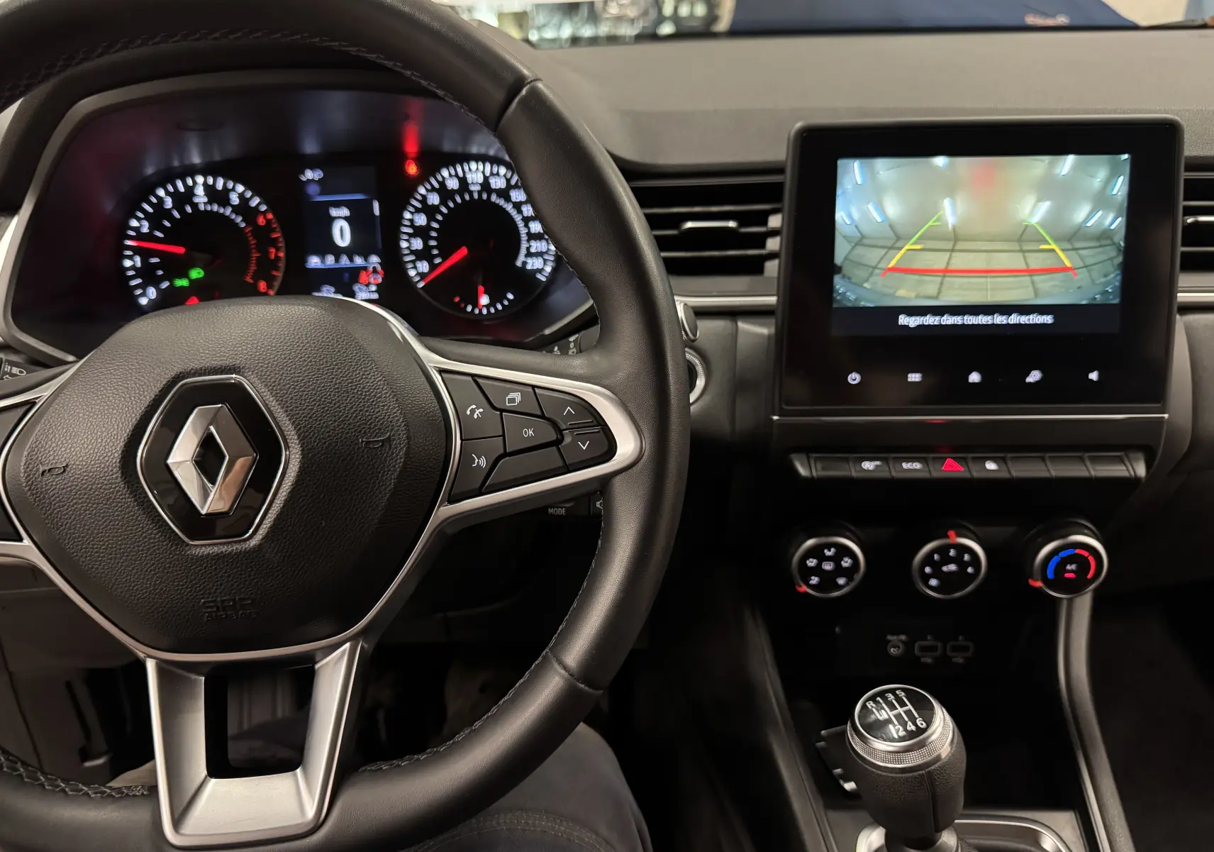 Vue intérieure du tableau de bord du Renault Captur 2021 avec volant, écran de caméra de recul et levier de vitesse manuel.