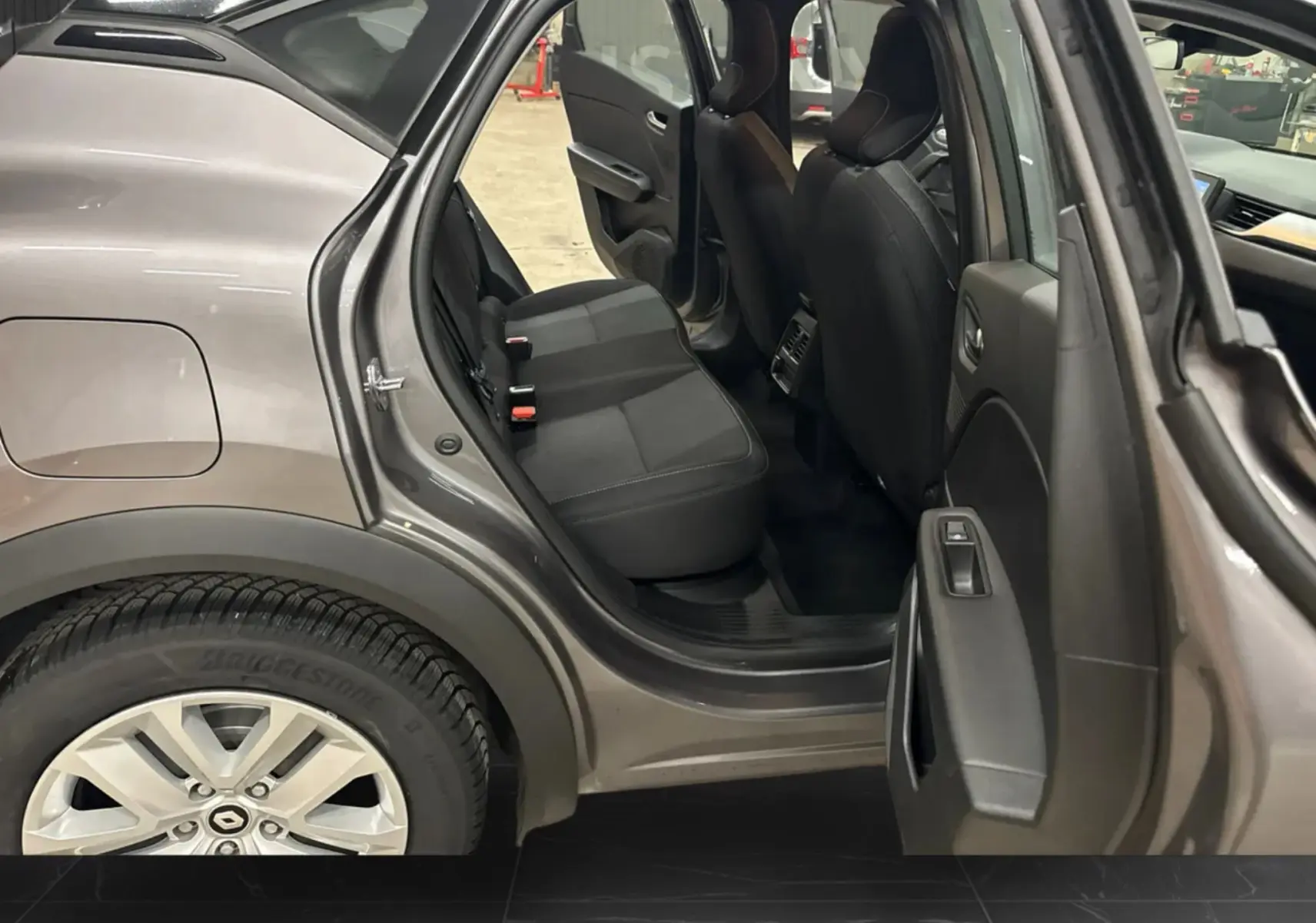 Vue côté gauche arrière du Renault Captur gris foncé avec porte arrière ouverte, montrant l'intérieur noir des sièges arrière.