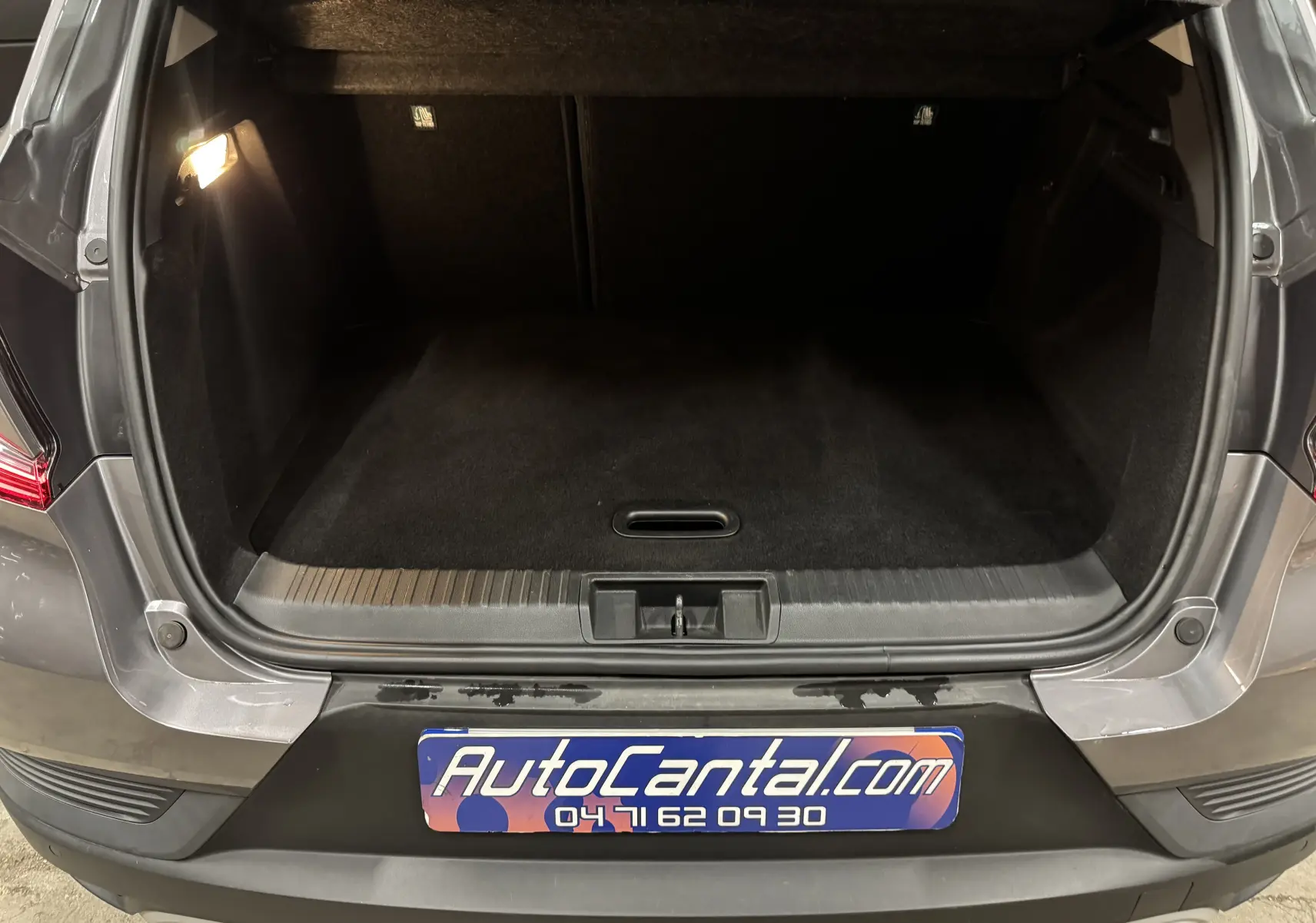 Coffre ouvert vu de l’arrière d’un Renault Captur gris foncé avec toit noir, montrant l’espace de chargement vide et éclairé.