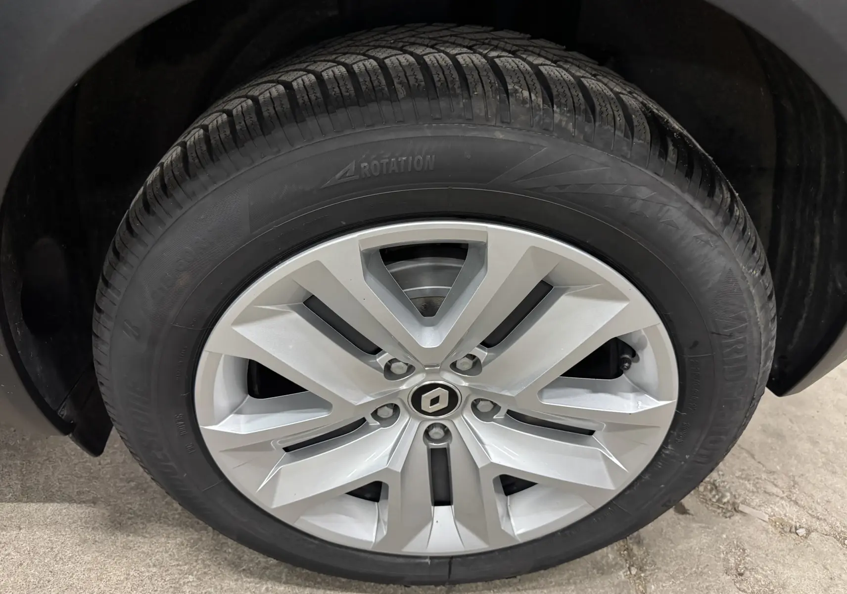 Gros plan sur la roue avant droite du Renault Captur gris foncé, mettant en valeur la jante argentée au design moderne.