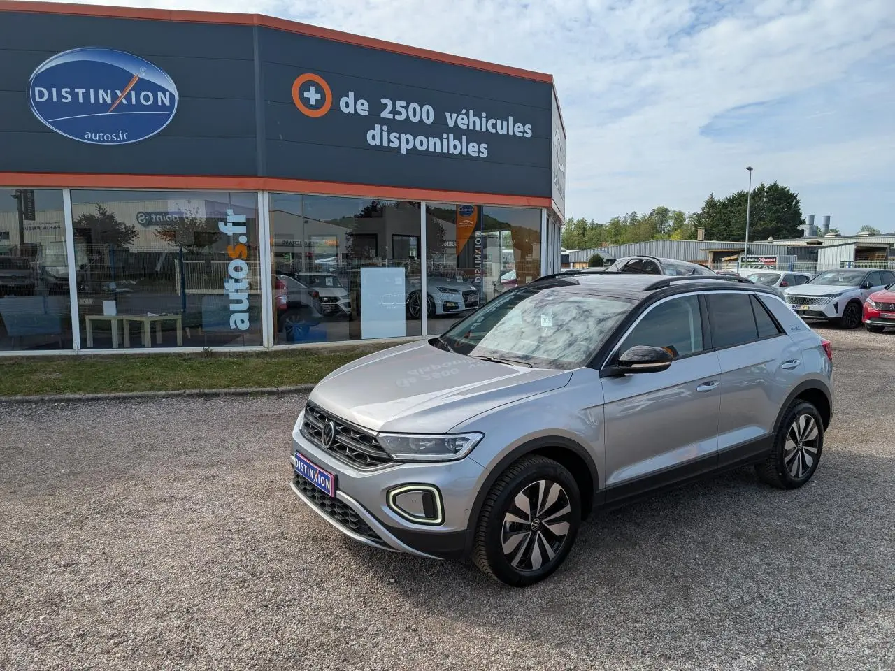 Volkswagen T-Roc gris 3/4 avant droit avec toit noir et jantes alliage 17 pouces, stationné devant un showroom.