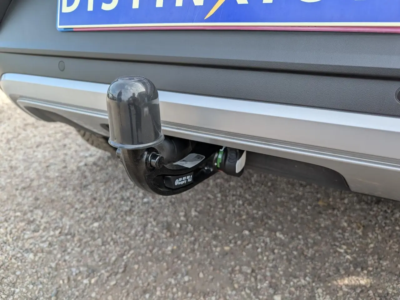 Gros plan sur l'attelage amovible noir fixé au pare-chocs arrière gris métallisé du Volkswagen T-Roc 2025.